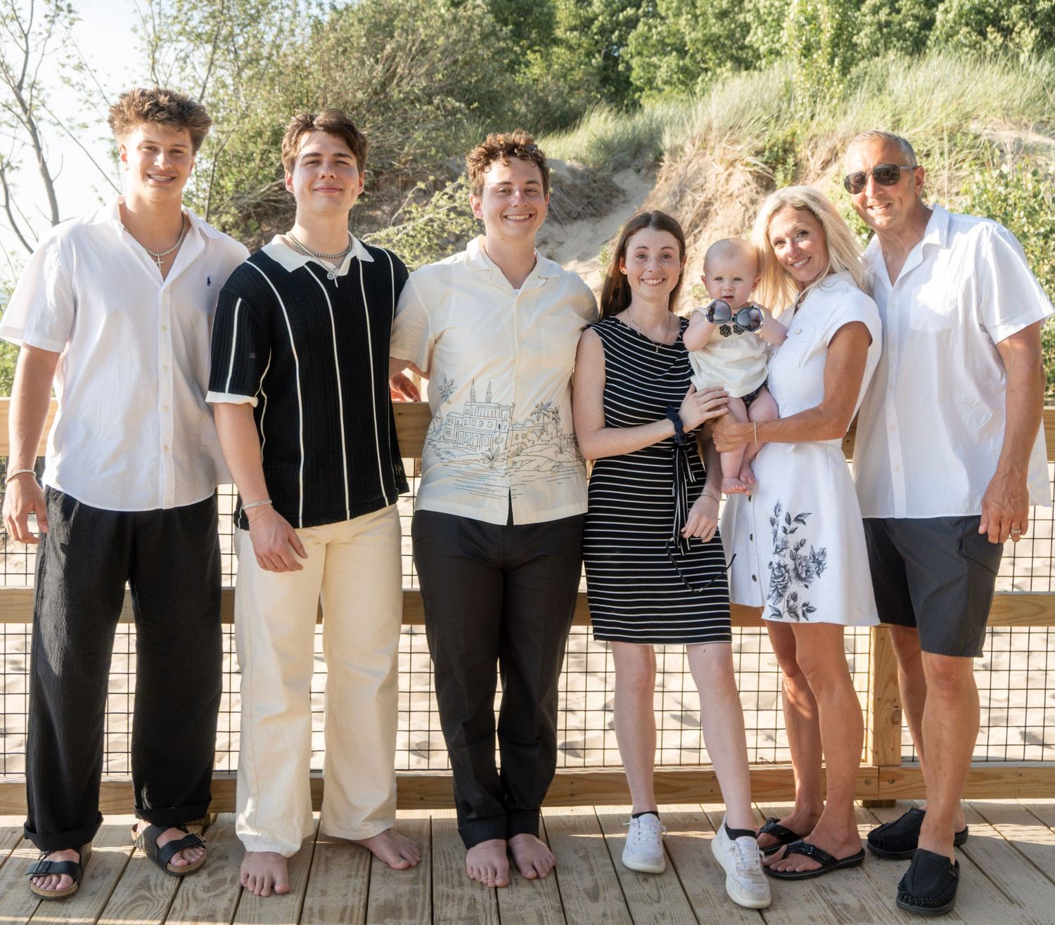 Family of seven posing together on a wooden deck outdoors, smiling for a group portrait on a sunny day.