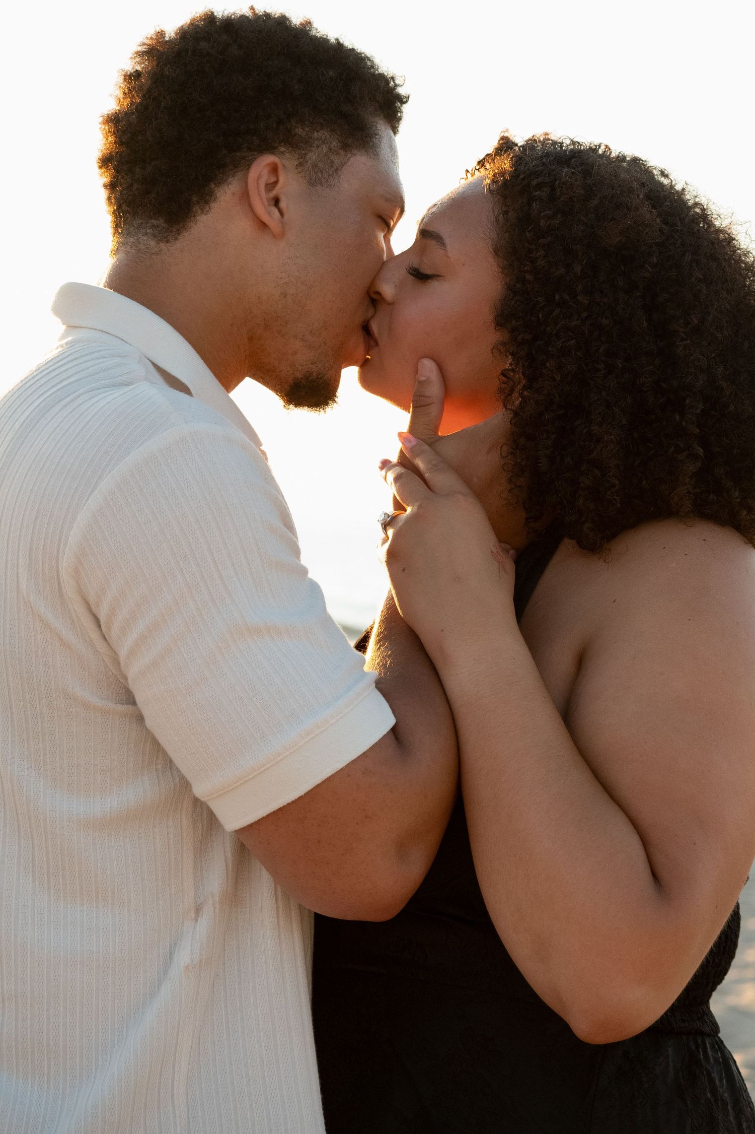A couple sharing a romantic kiss outdoors at sunset, woman touching man's face tenderly.