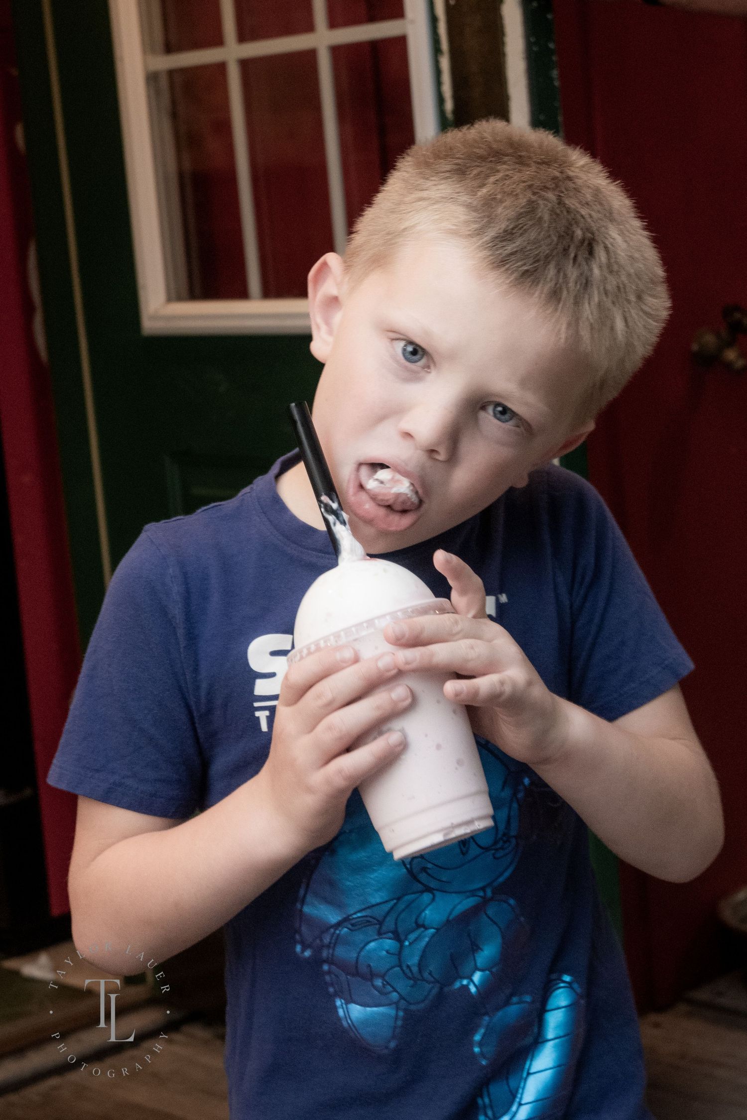 Blonde boy in blue Sonic t-shirt making a funny face while holding a milkshake with a straw.