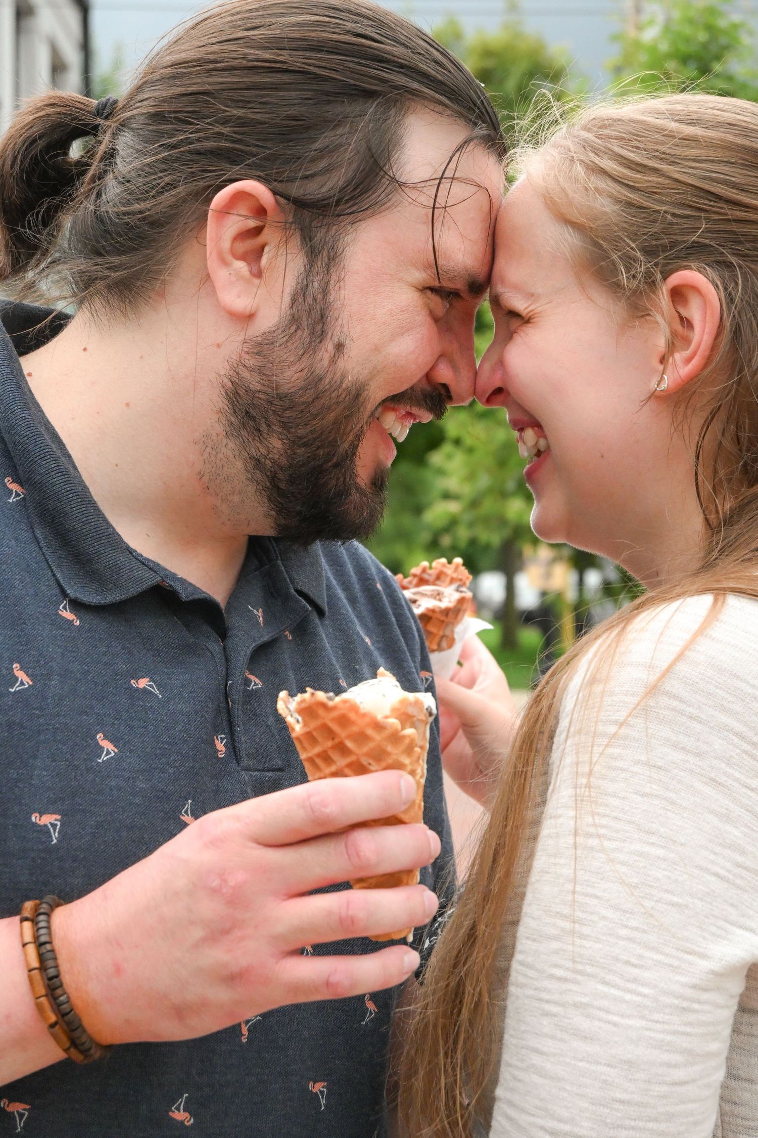 A happy couple touching foreheads and smiling while each holding a waffle ice cream cone outdoors.