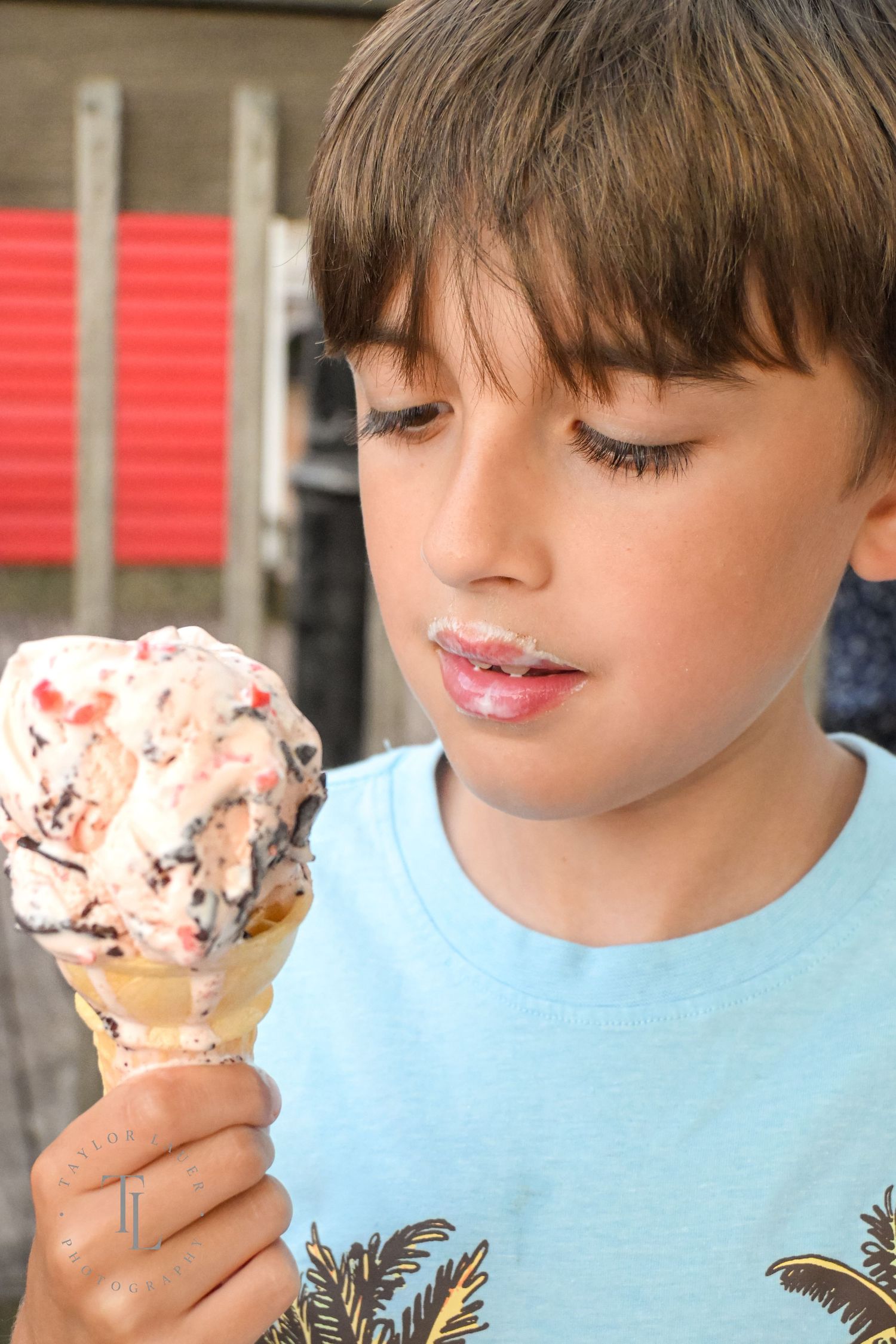 A young boy in a blue shirt gazes at a melting ice cream cone he is holding.