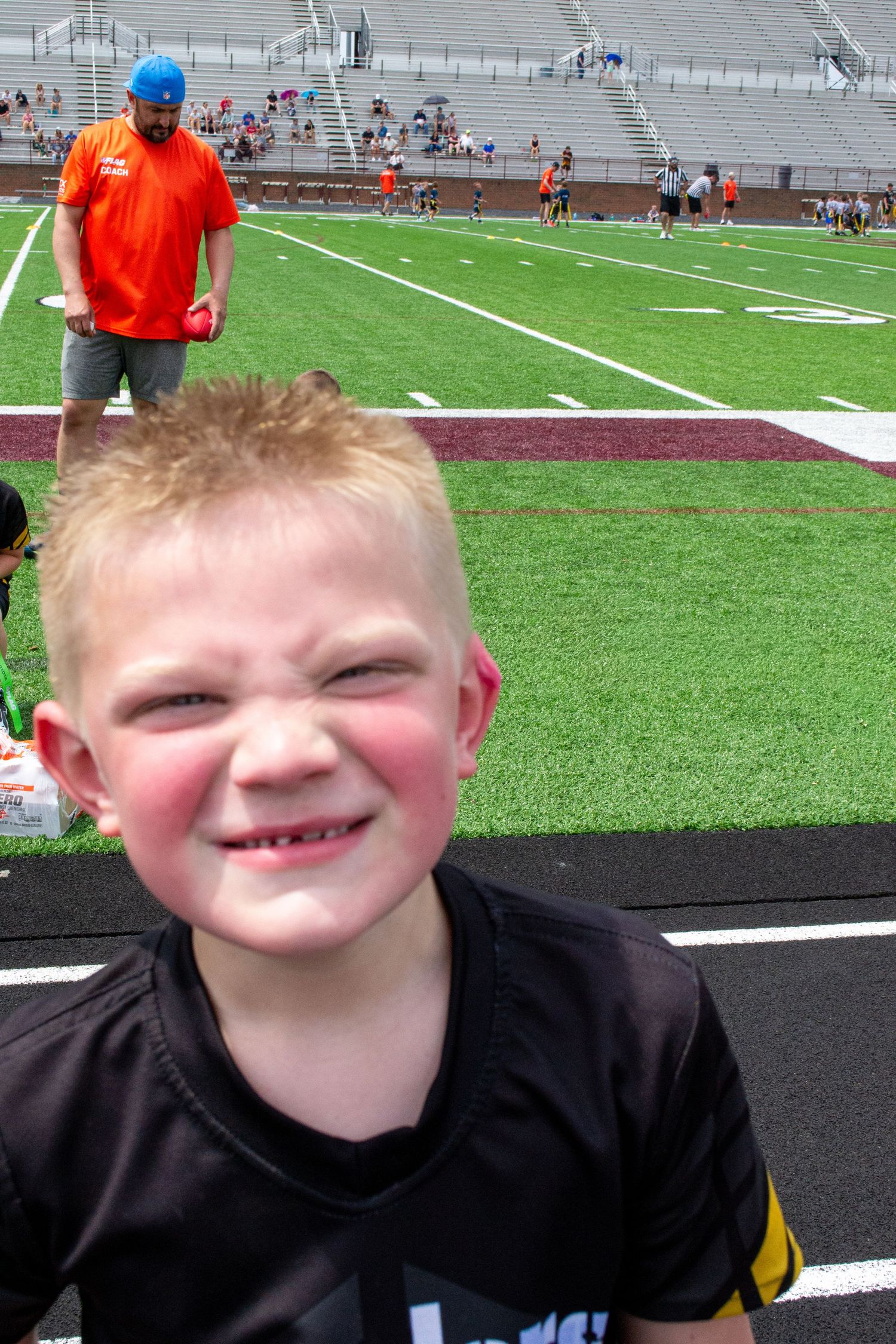 Smiling young boy with missing teeth at a youth flag football game on turf field.