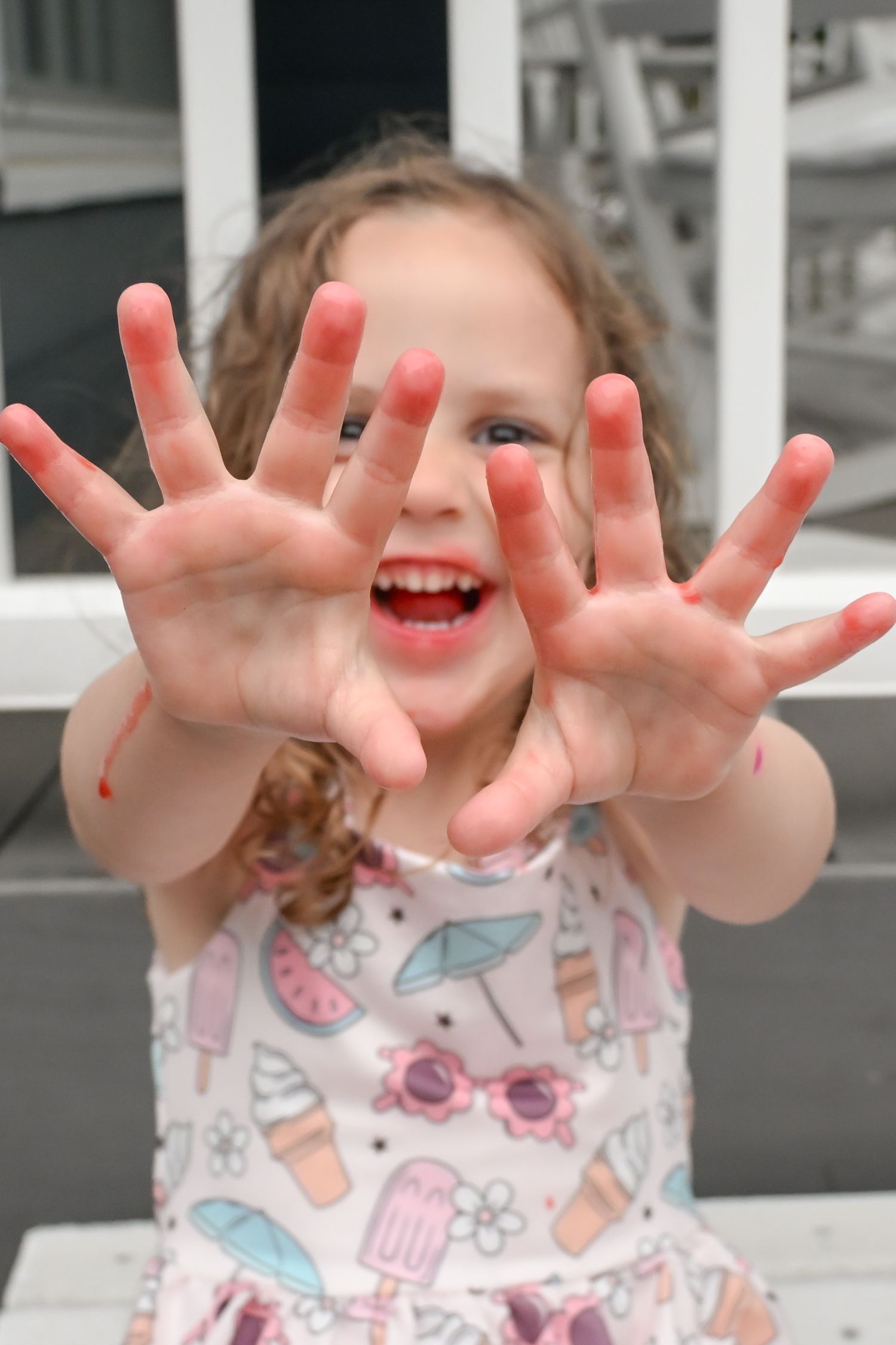 Excited young girl shows off her red-stained hands while smiling brightly.