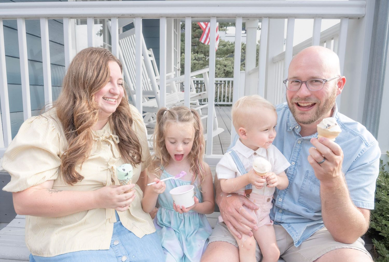 Happy family of four enjoying ice cream cones together on a porch steps on a sunny day.