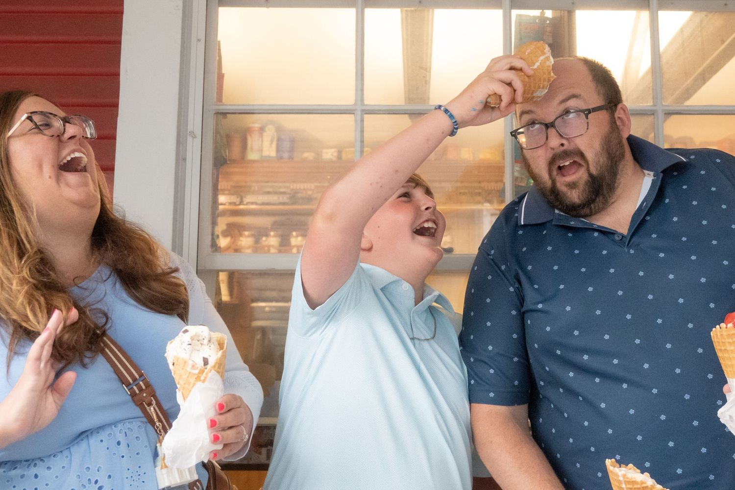 Family laughs as young boy dramatically tosses ice cream cone in the air.