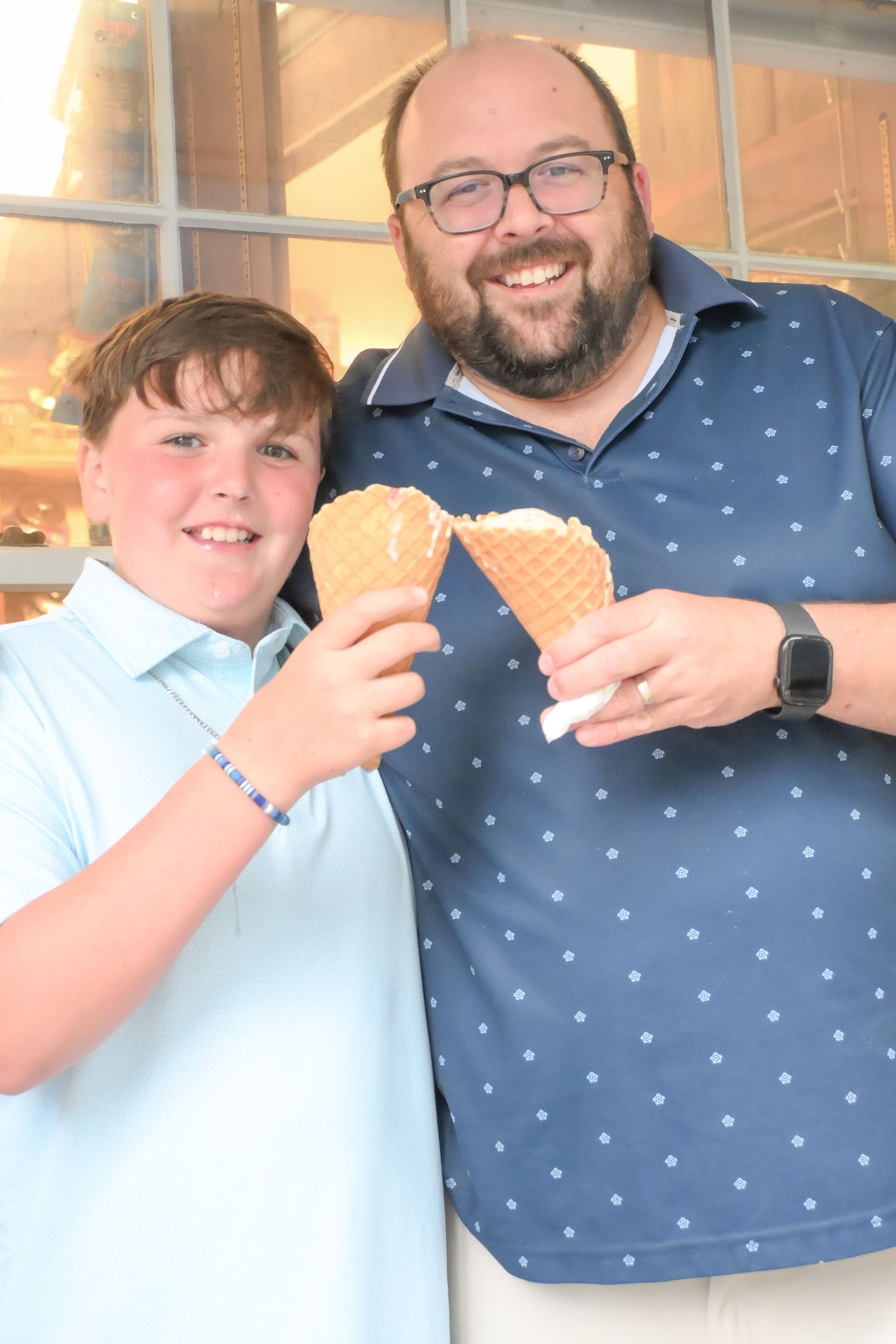 Smiling boy and father pose together holding matching waffle cone ice creams.