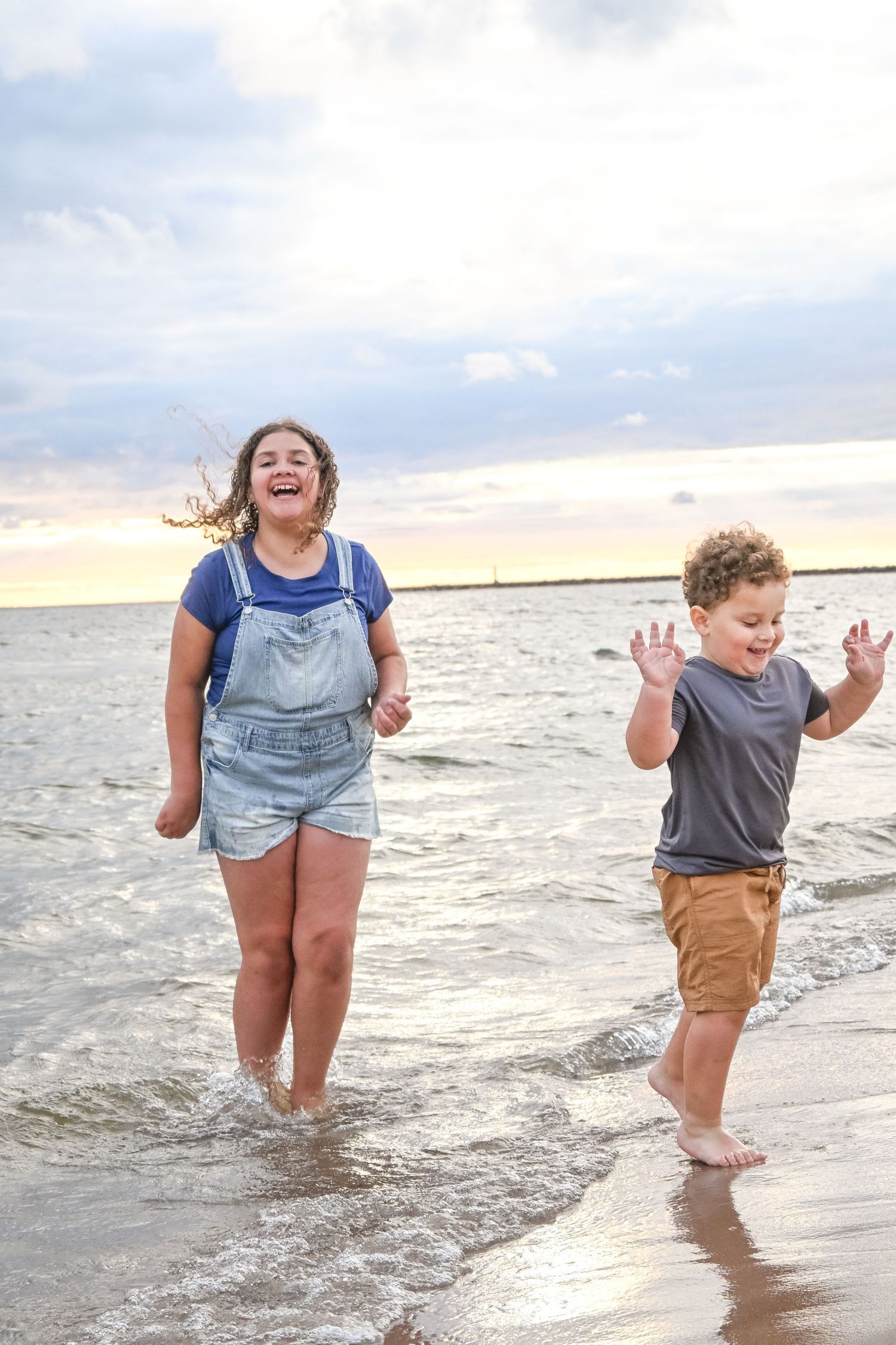 Two children laugh and splash joyfully in ocean waves at sunset on the beach.