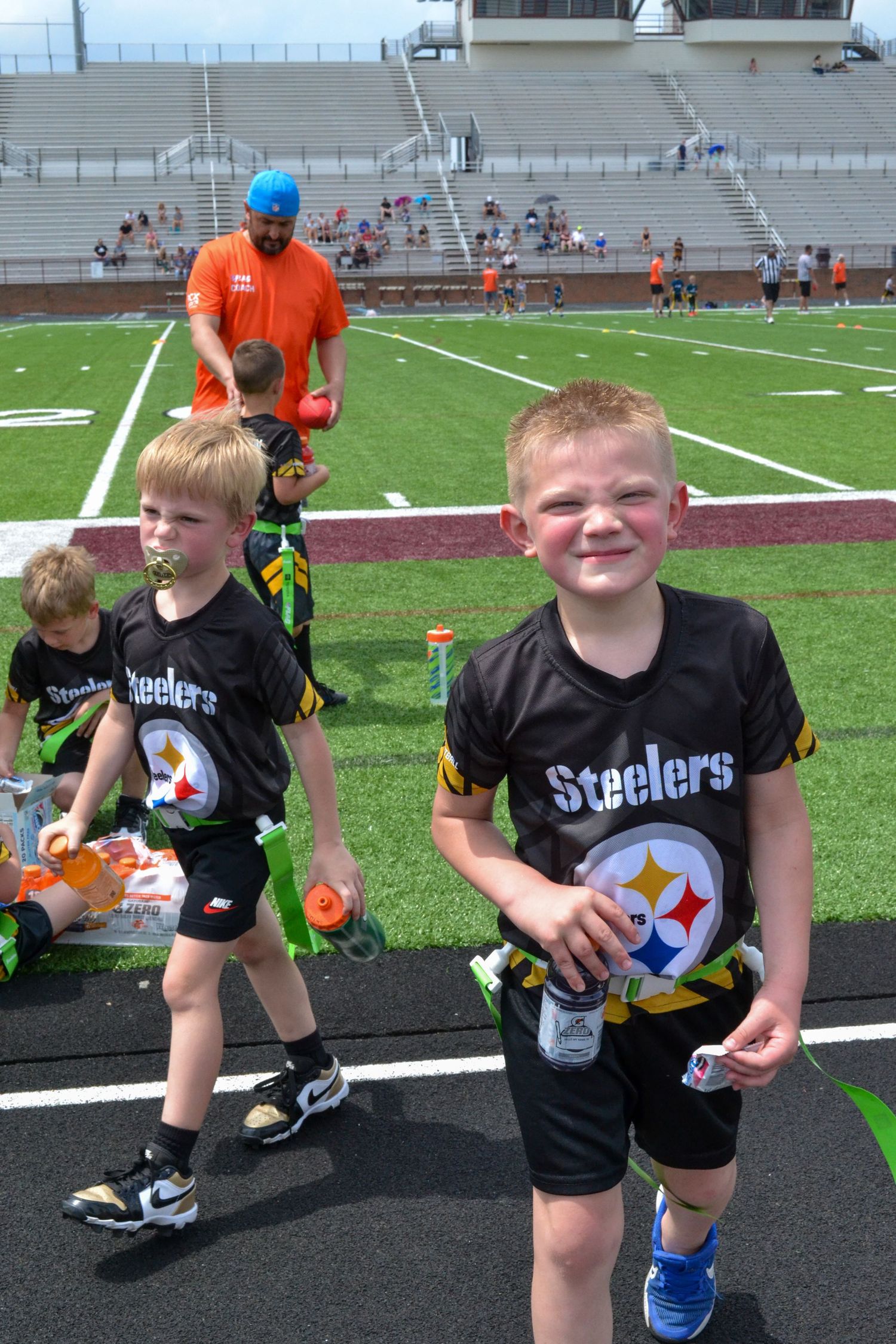 Two young boys in Pittsburgh Steelers black jerseys smiling on a football field during a youth game.