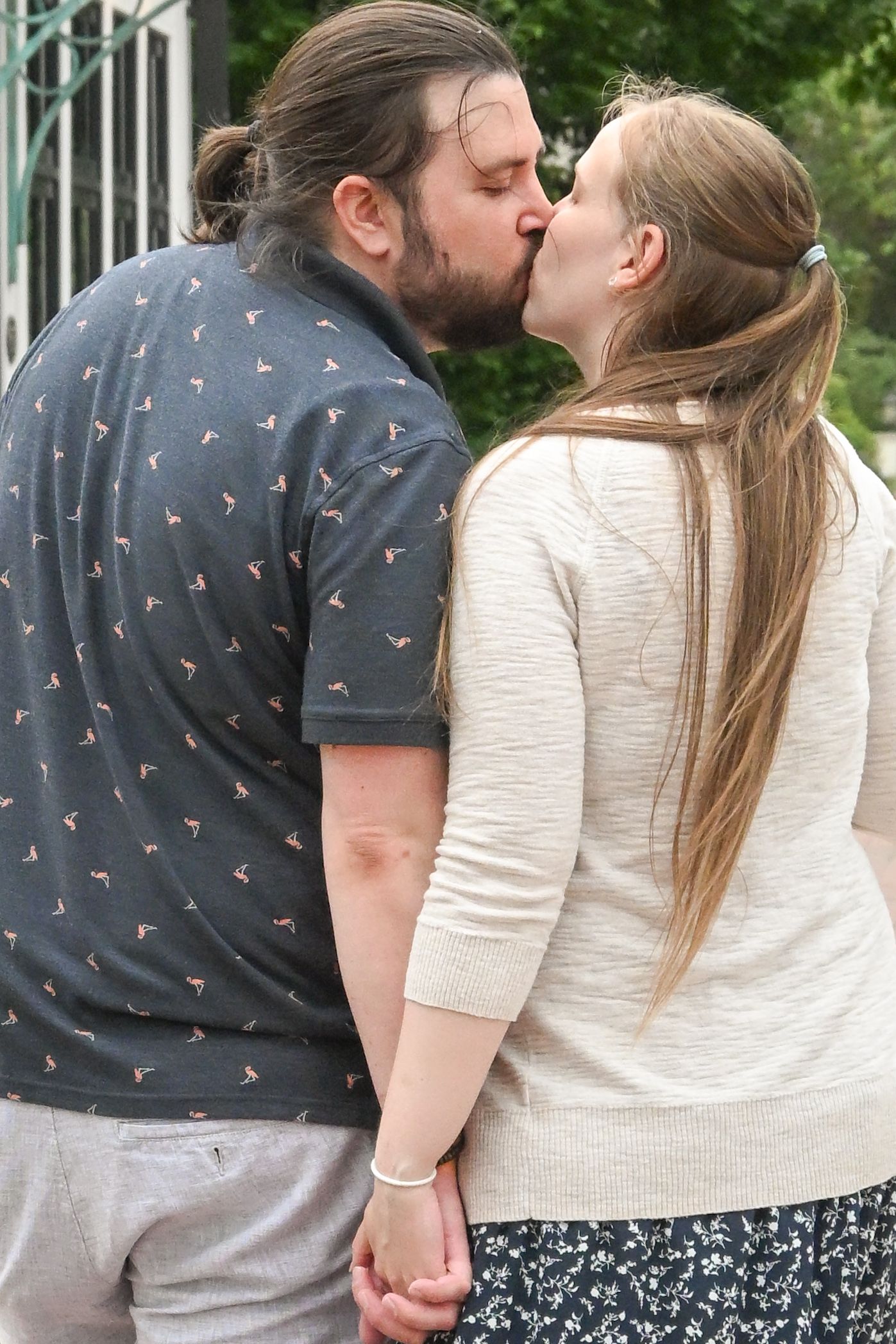 A couple holding hands and sharing a romantic kiss outdoors on a sunny day.