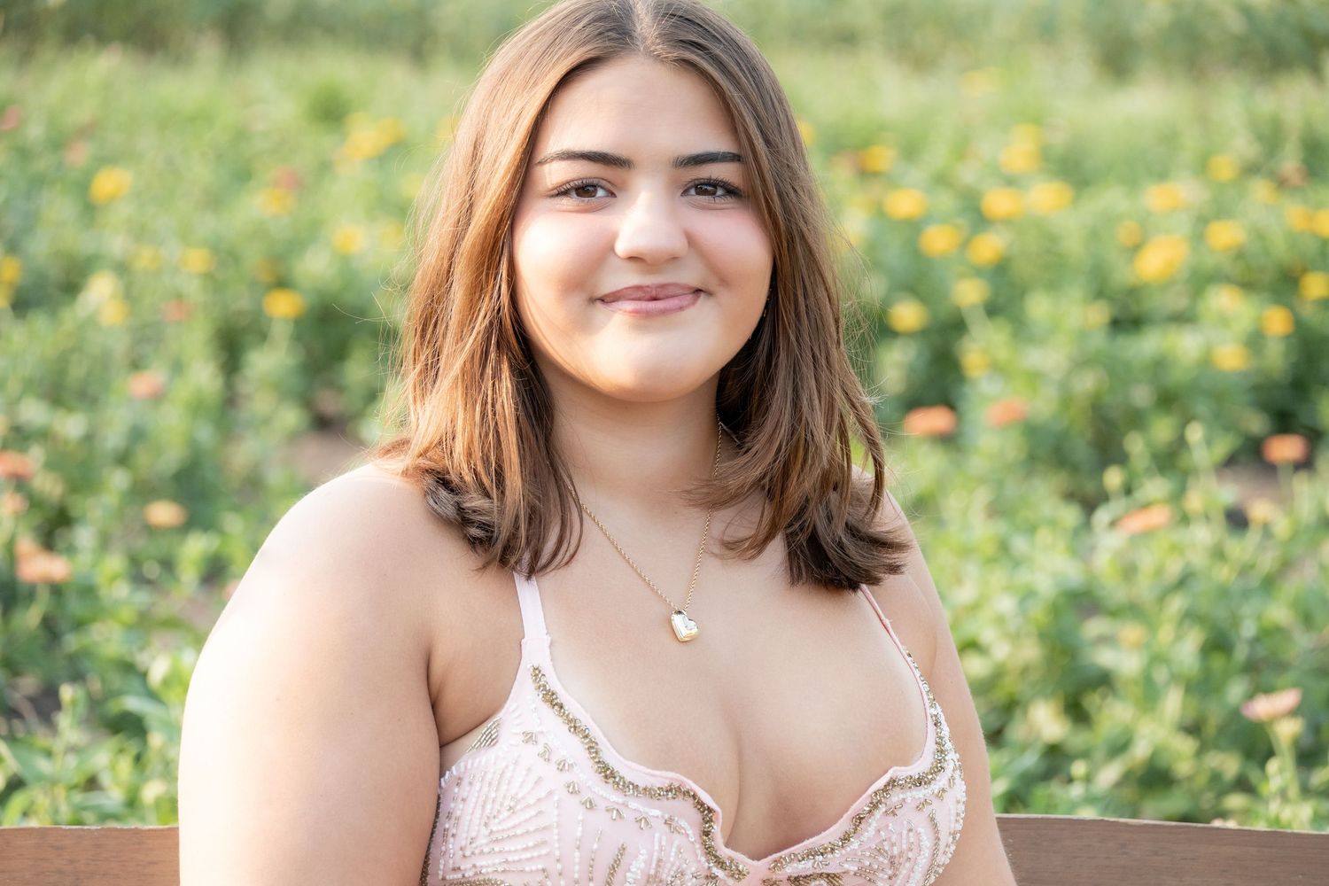 Young woman smiling outdoors in a floral field, wearing a lace top and delicate necklace, soft natural lighting.