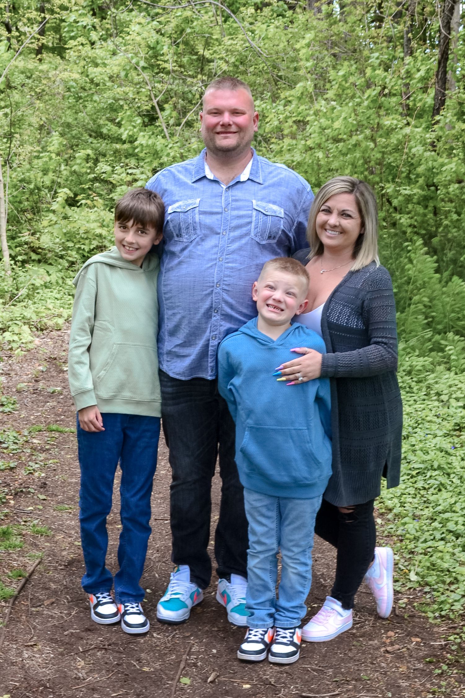 Family of four posing together on a nature trail surrounded by lush green foliage.
