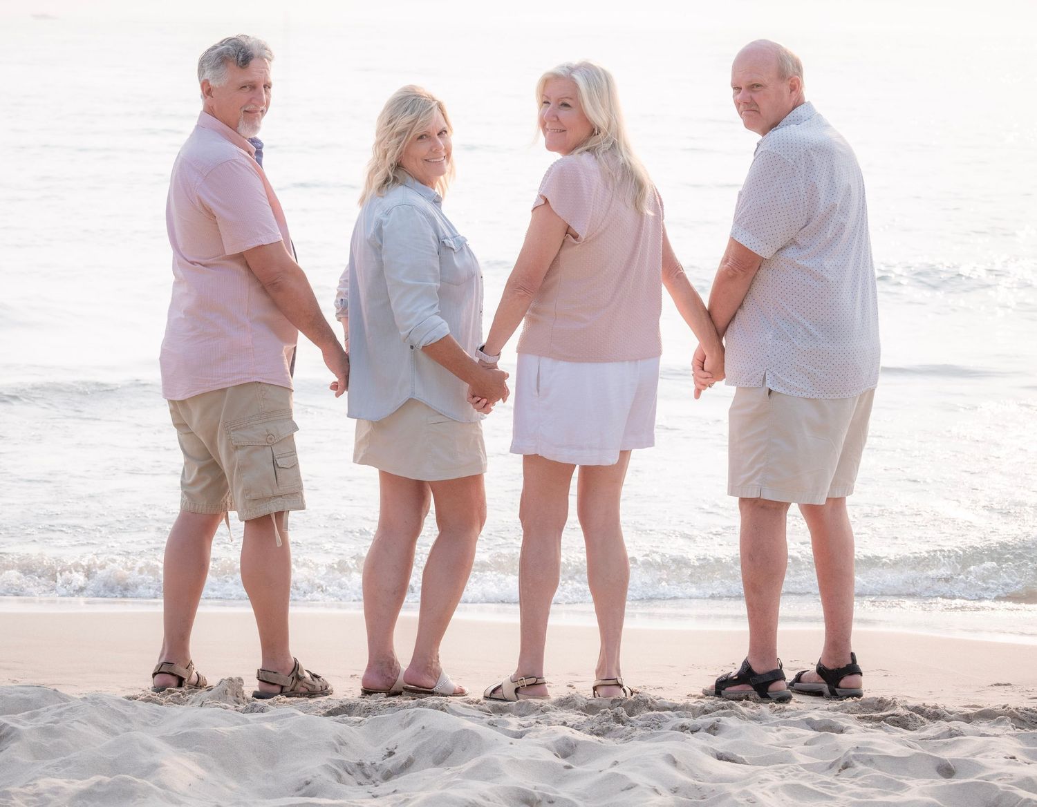 Four adults holding hands on a sandy beach with ocean waves in the background during golden hour.