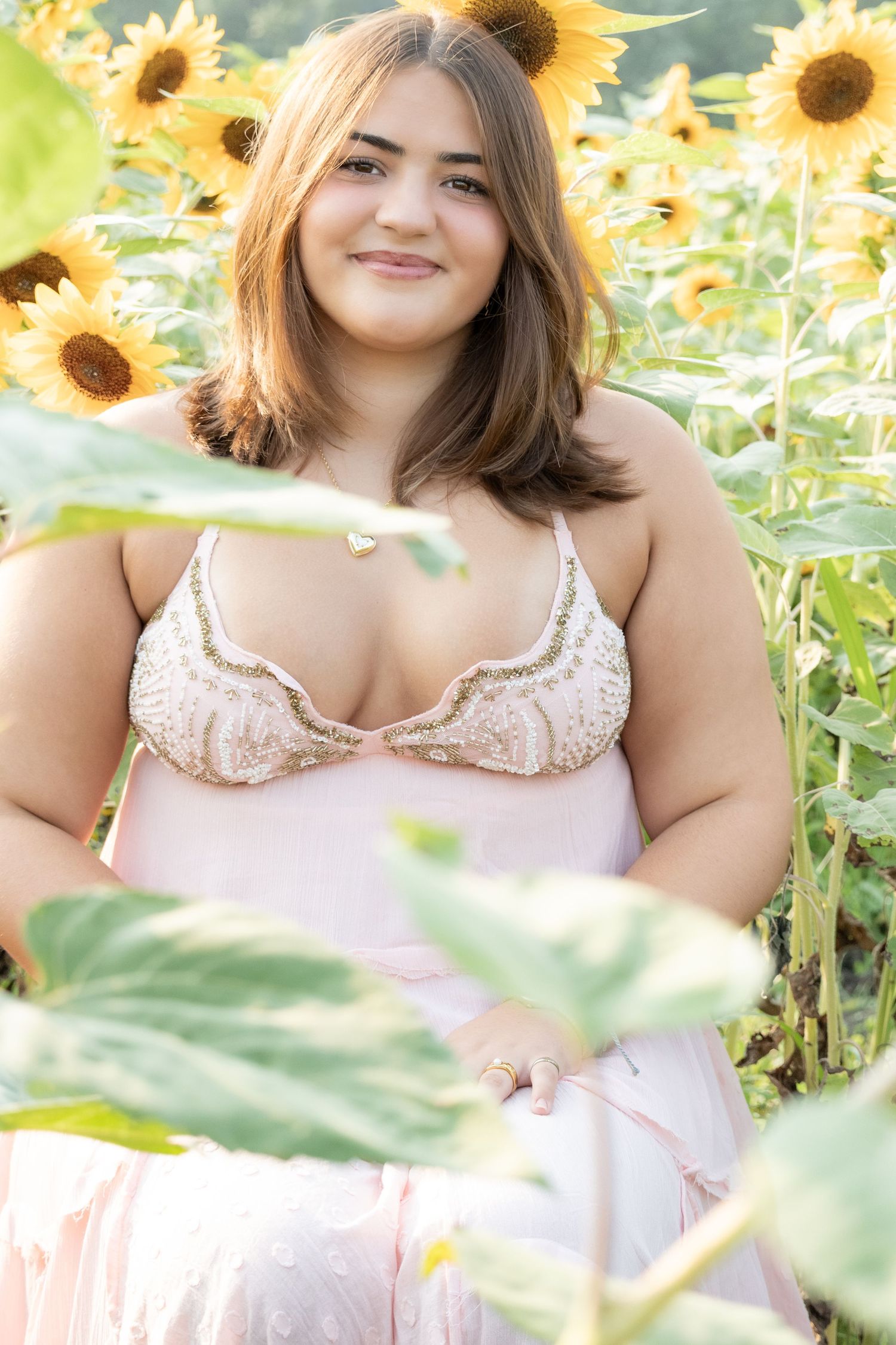 Young woman in pink lace top smiling among vibrant sunflowers in a sunny field.