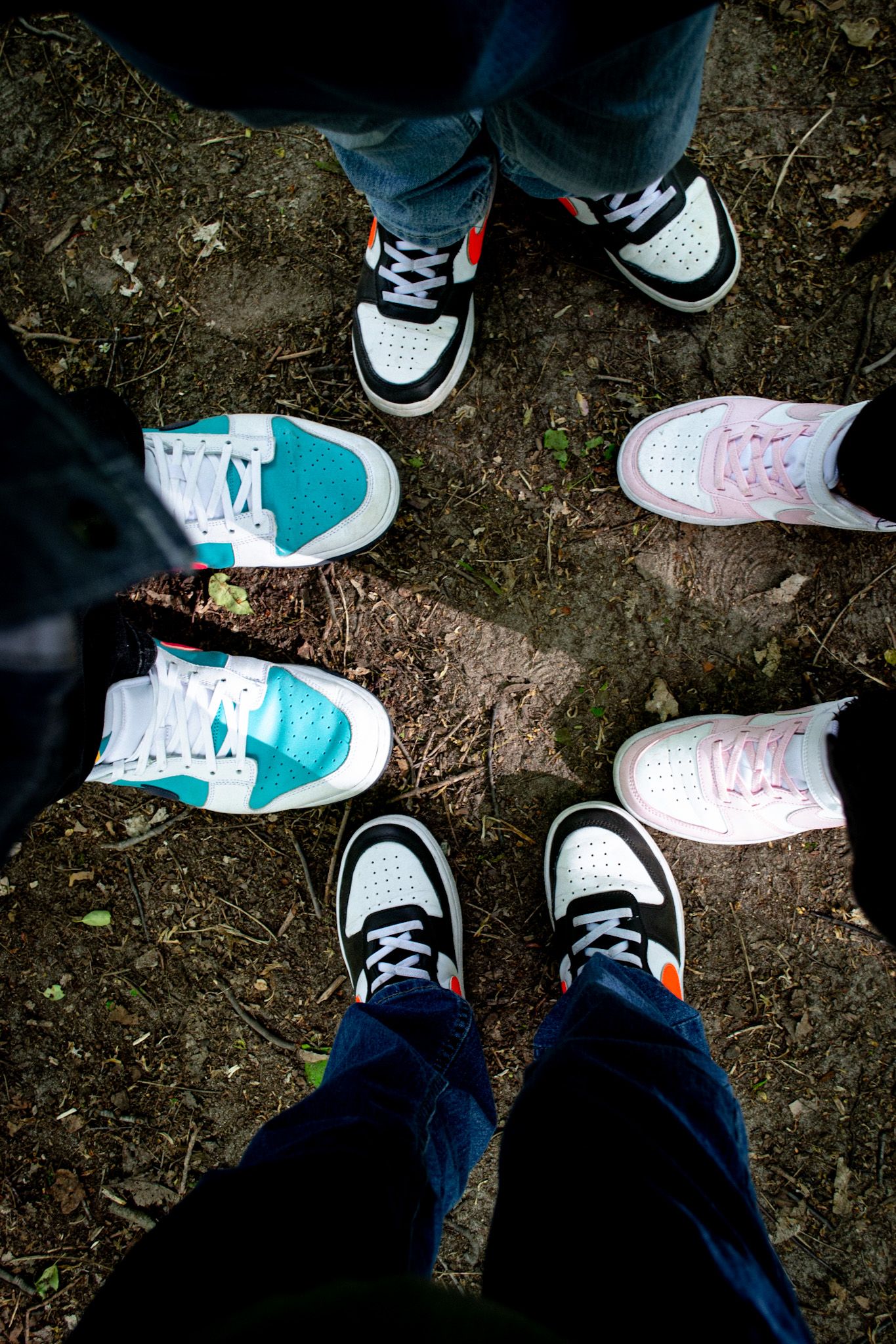 Overhead view of four people standing in a circle showing off colorful Nike sneakers on a dirt ground.