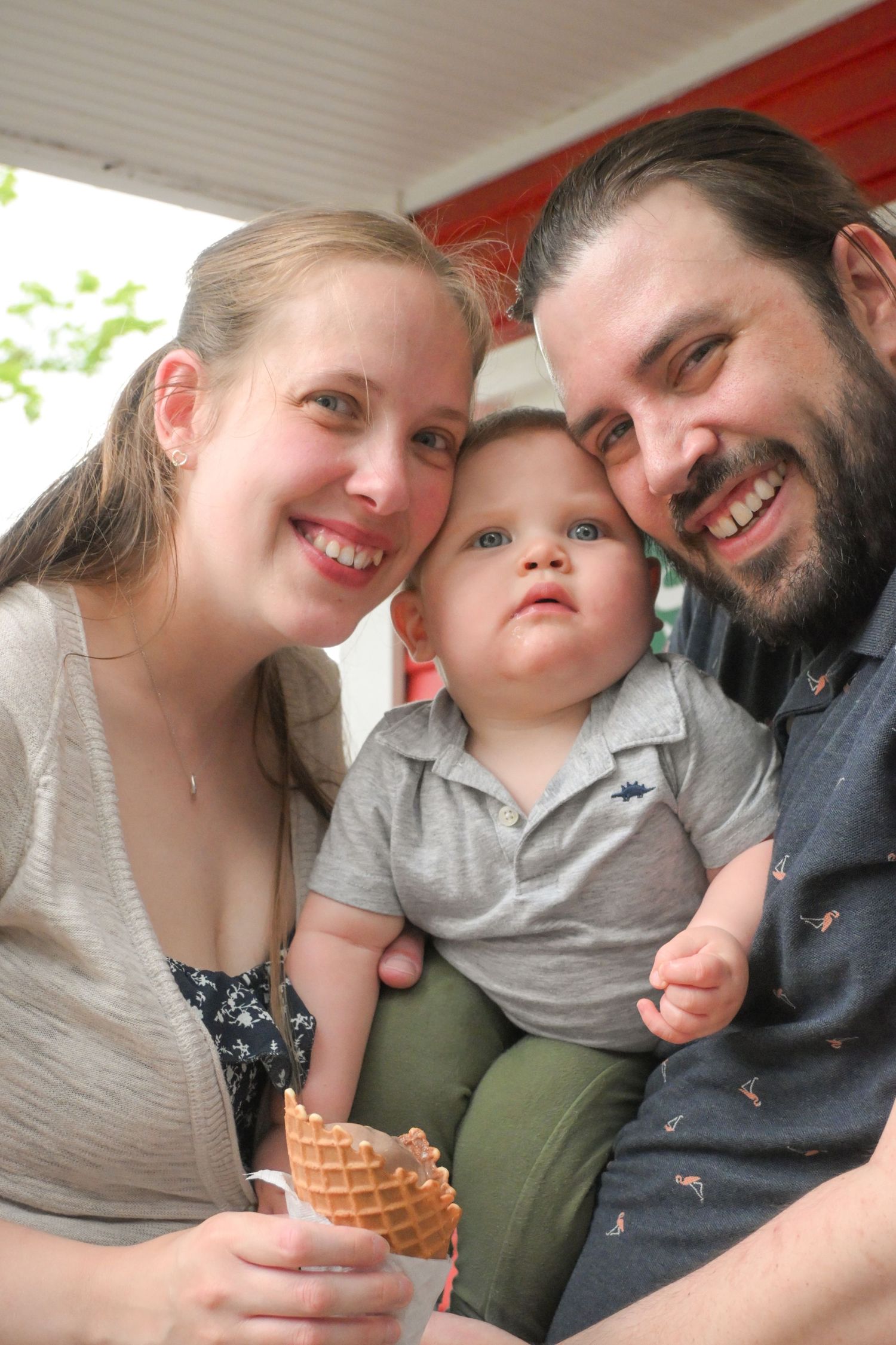 A smiling family with a blue-eyed baby boy posing together with a waffle cone ice cream treat.