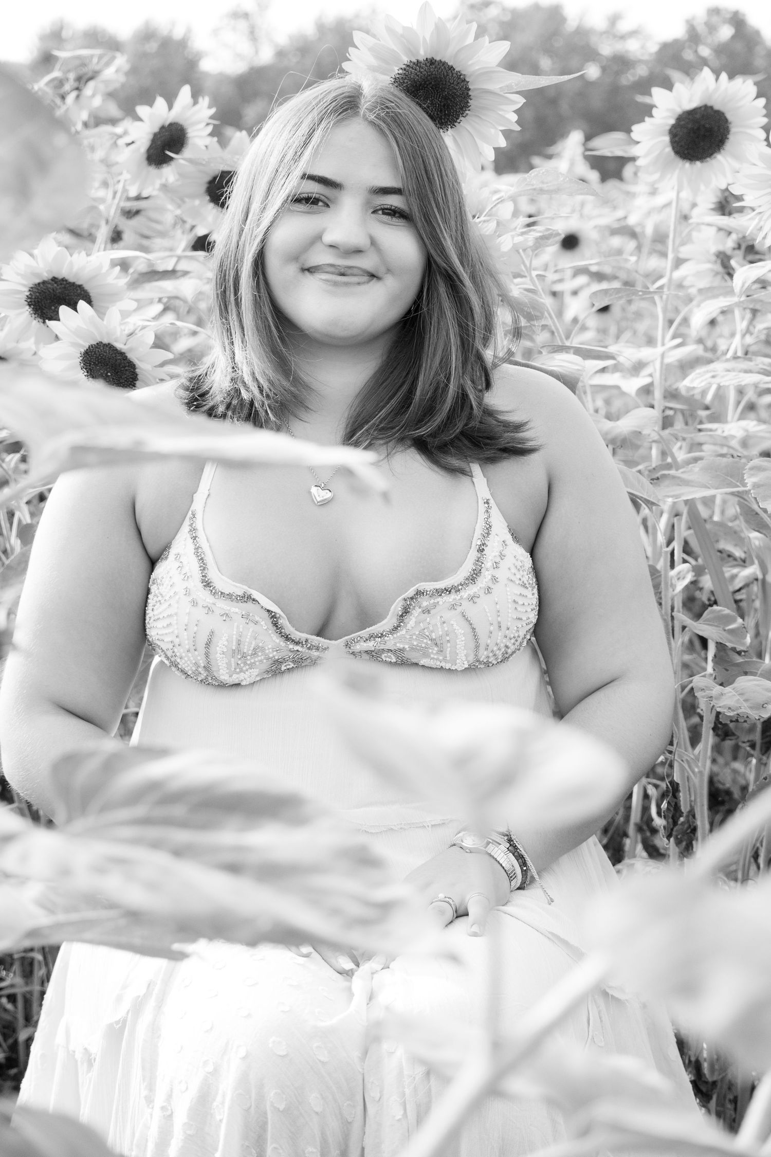 Young woman smiling in a sunflower field, wearing a white dress, black and white portrait photography.