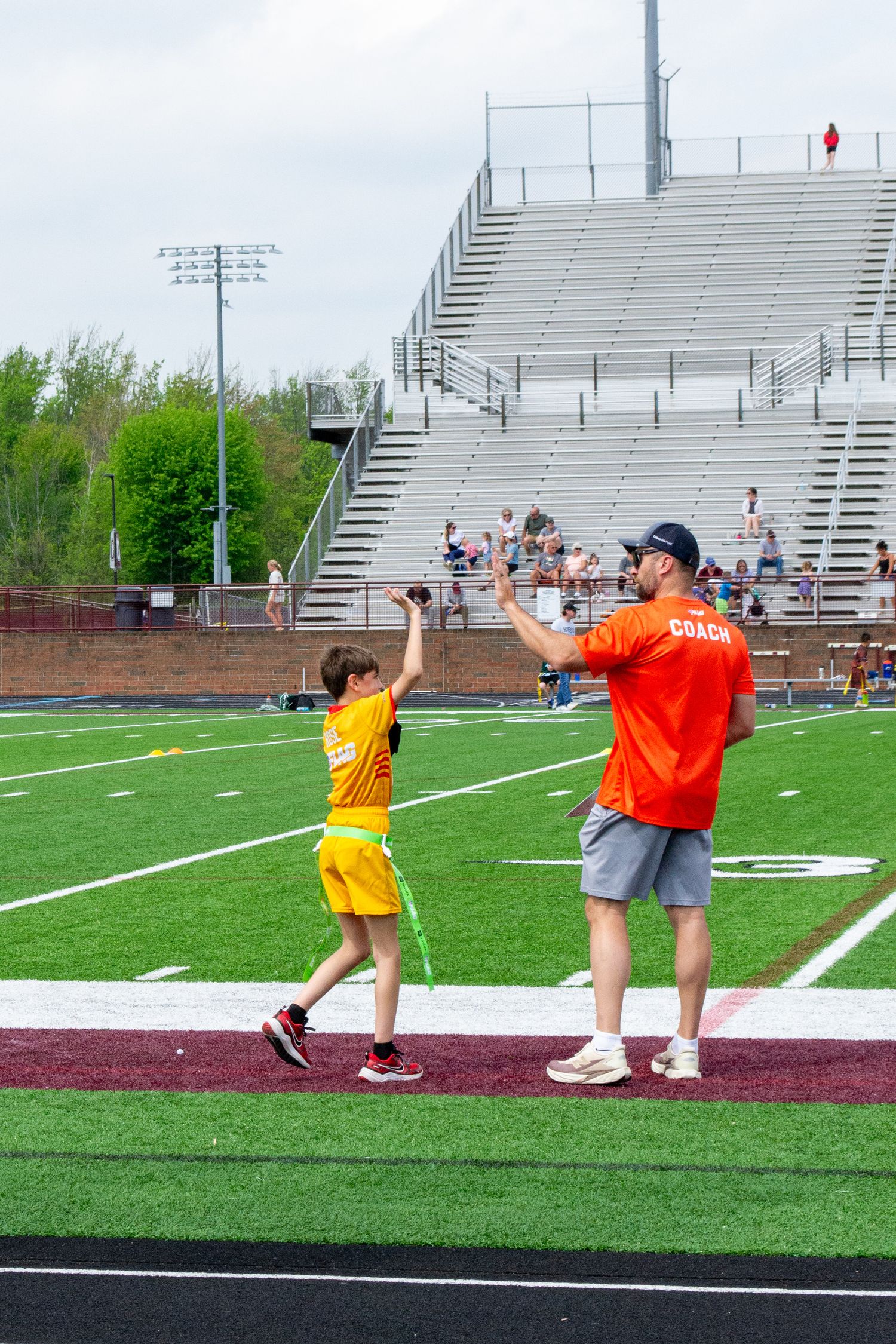 Youth flag football coach high-fiving young player in yellow uniform on green field.