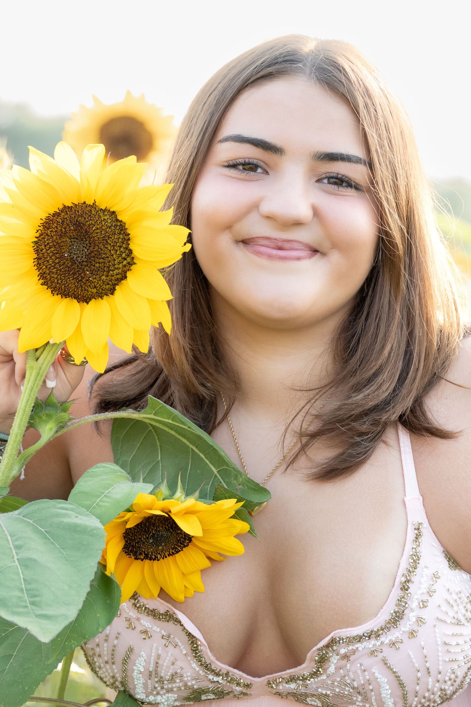Young woman smiling in a sunflower field, holding bright yellow sunflowers, wearing a lace top.