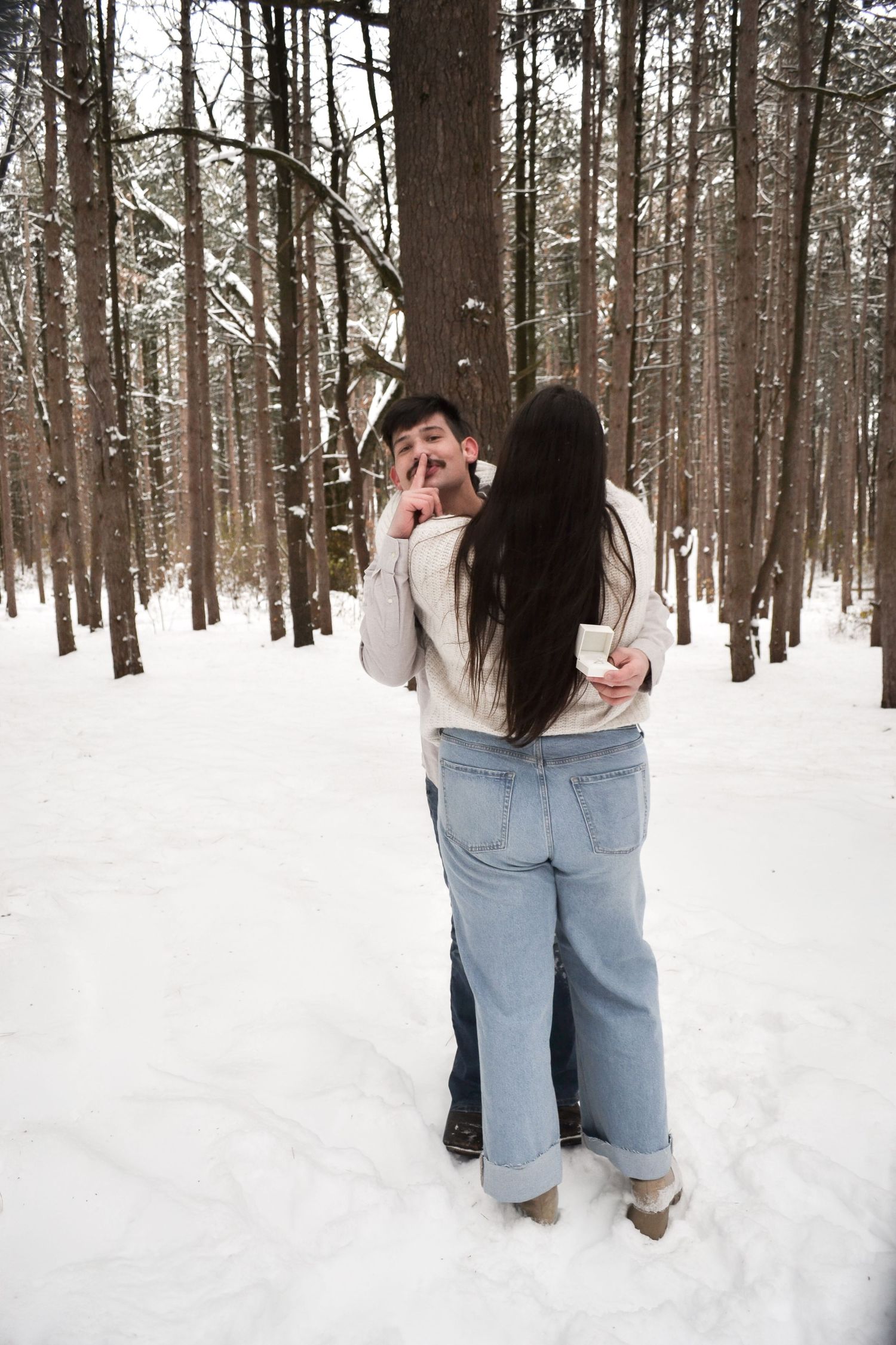 Couple sharing a tender kiss in a snow-covered pine forest during winter.