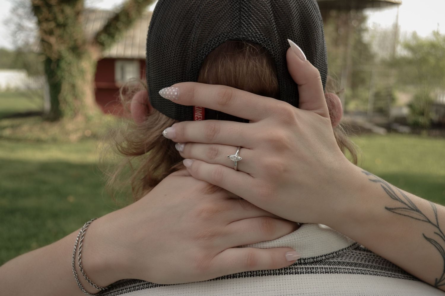 Close-up of a woman's hand with engagement ring resting on a man's neck during a romantic outdoor embrace.