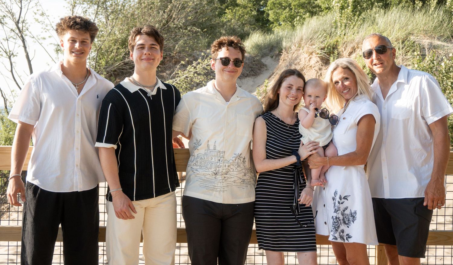 Group of seven people posing together outdoors on a sunny day, smiling for a family portrait photo.
