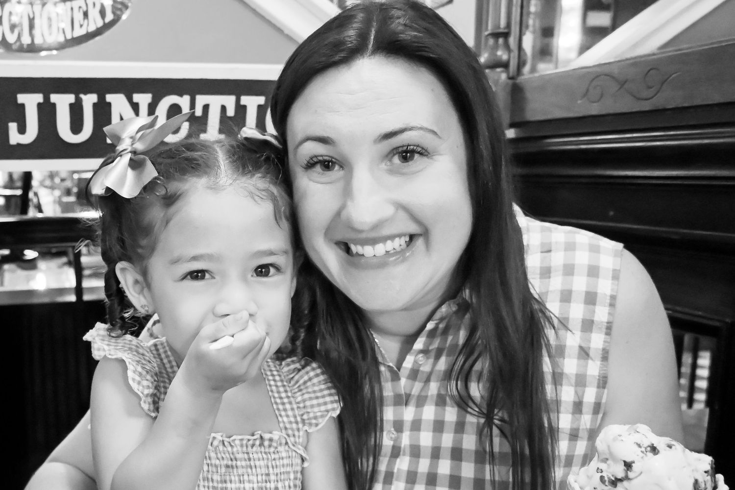 Black and white photo of a smiling mother and young daughter at an ice cream shop.