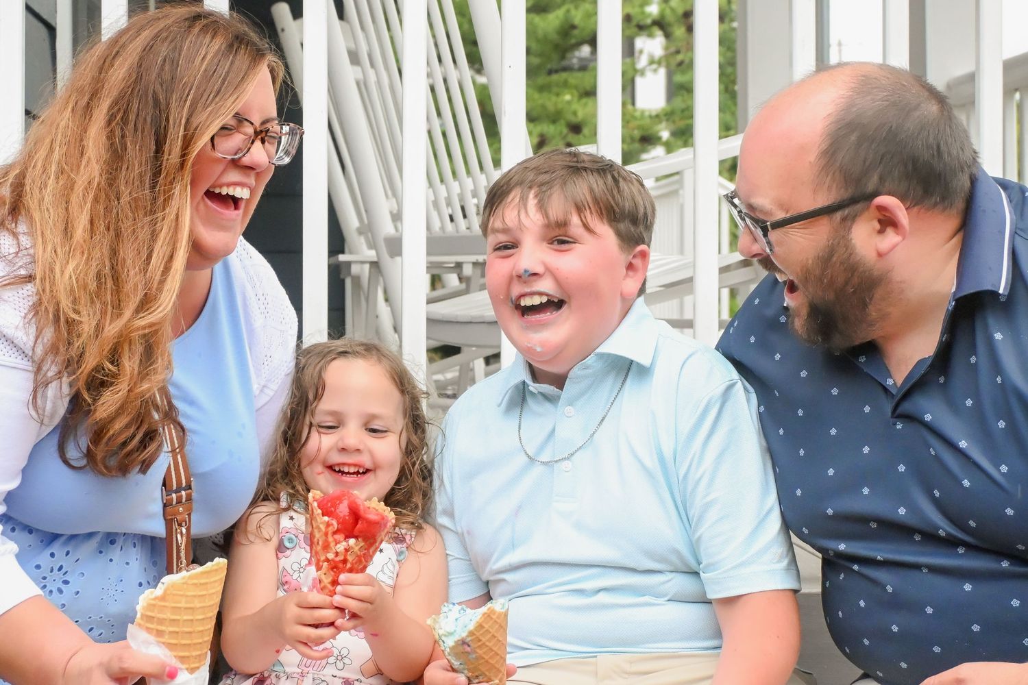 Happy family of four laughs together while enjoying ice cream cones outdoors.
