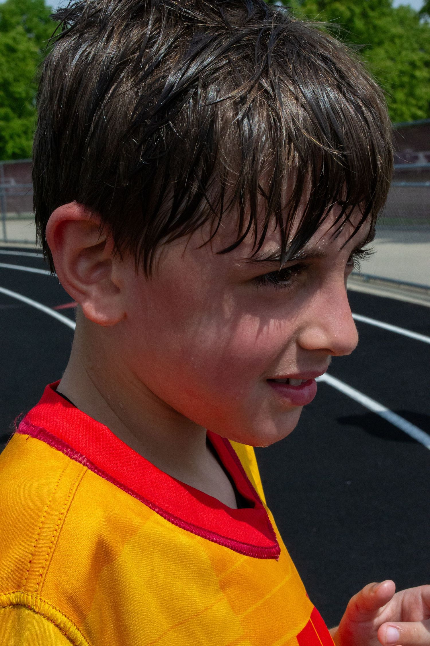 Sweaty young boy in yellow and red sports jersey smiling after an outdoor athletic event.