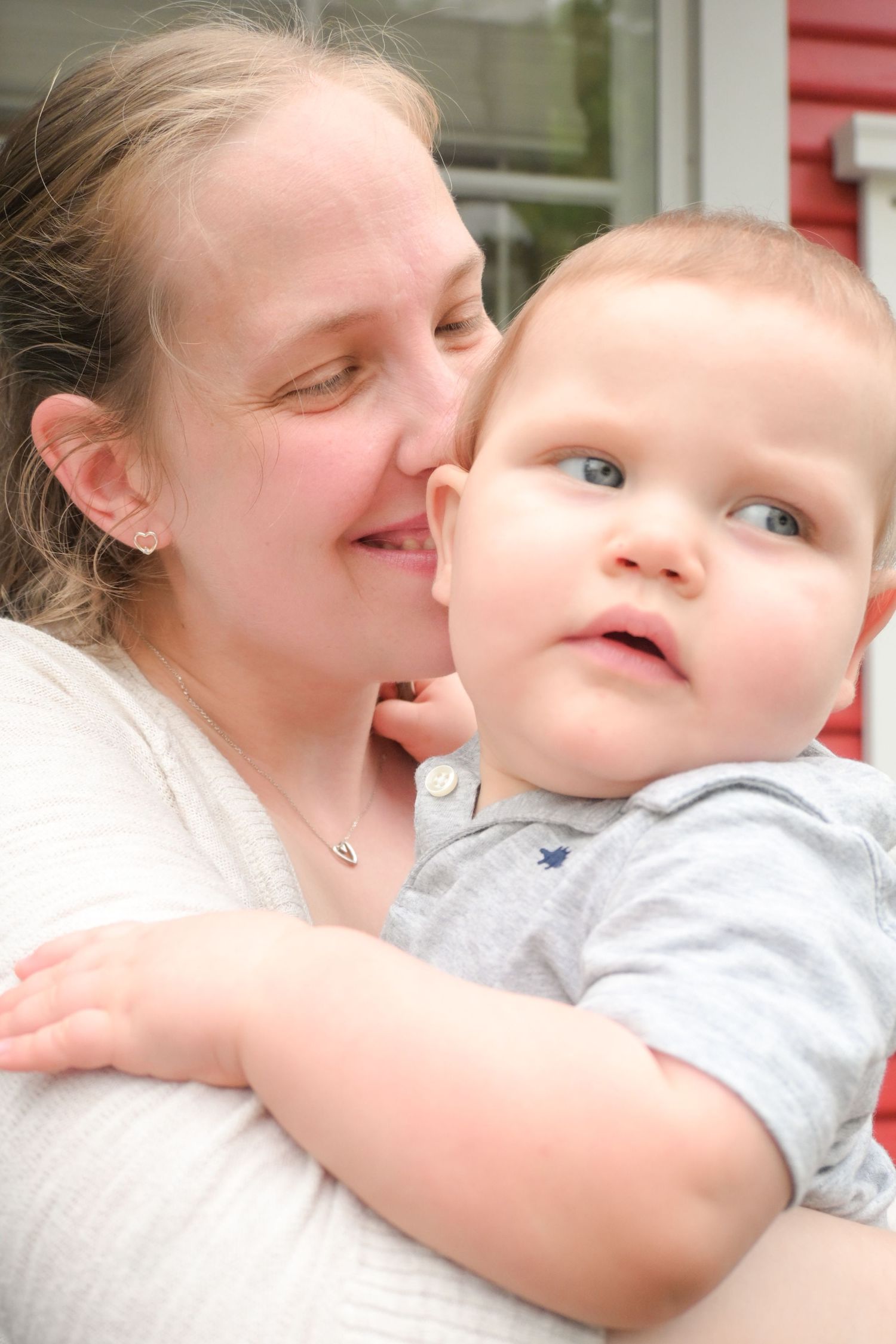 A loving mother gently kissing her blue-eyed baby boy on the cheek while holding him close.