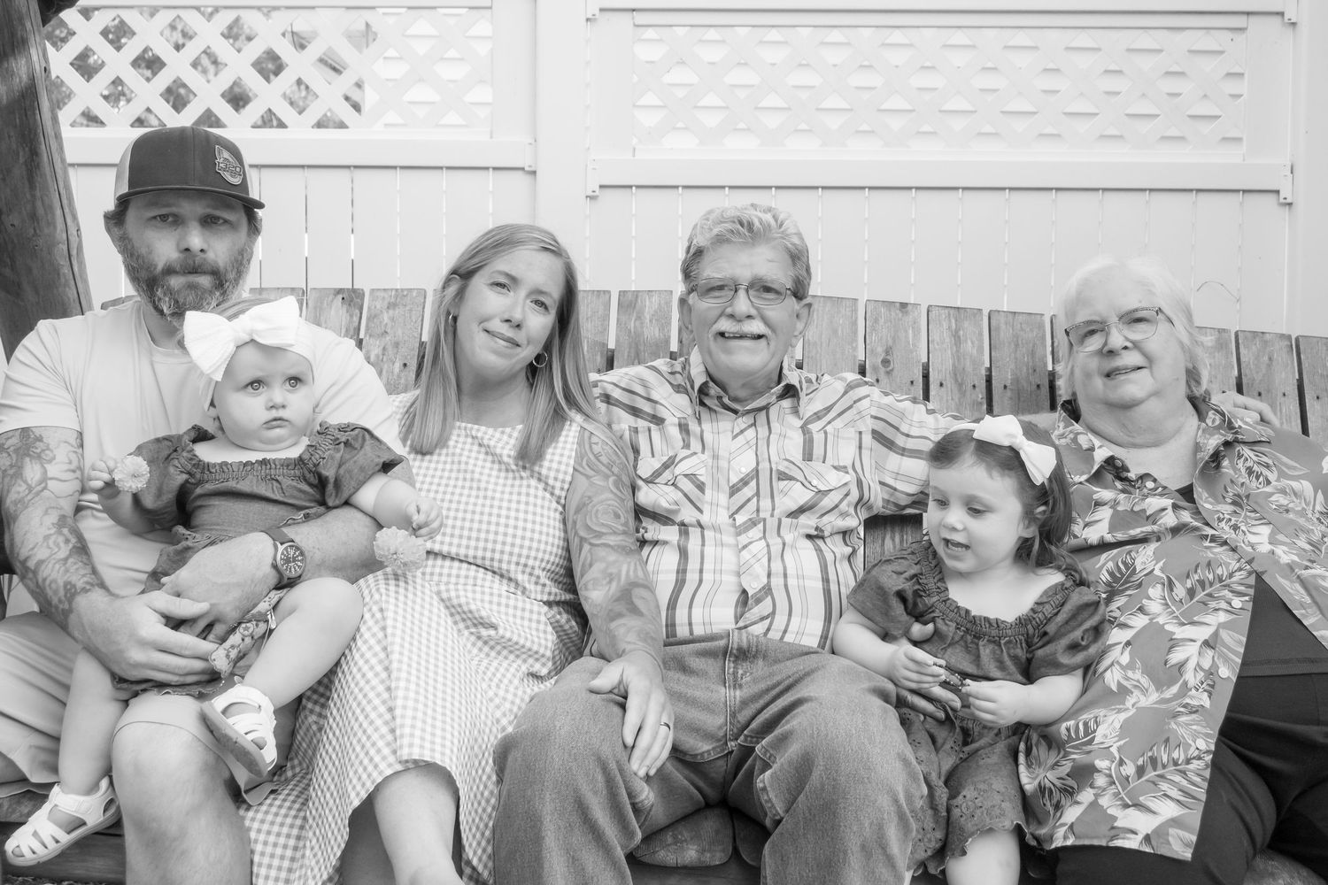 Black and white family portrait of six people including children posed together on a porch bench outdoors.