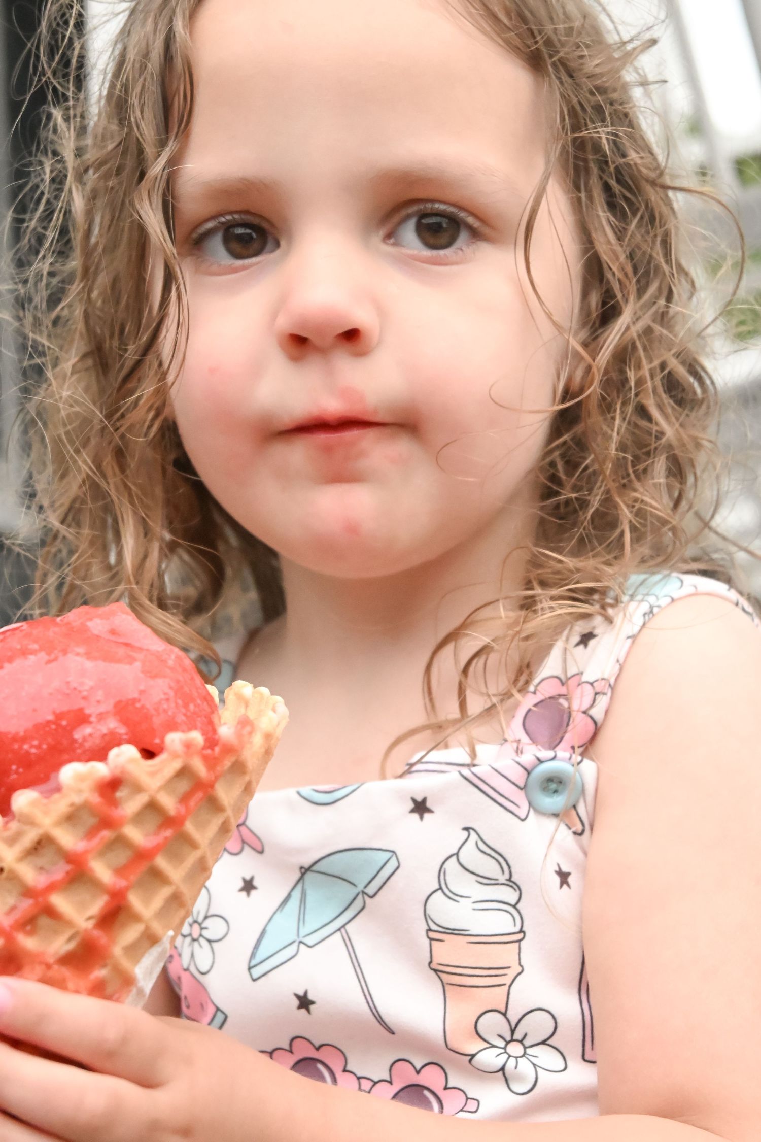 Adorable young girl with curly hair holds a strawberry waffle cone ice cream.