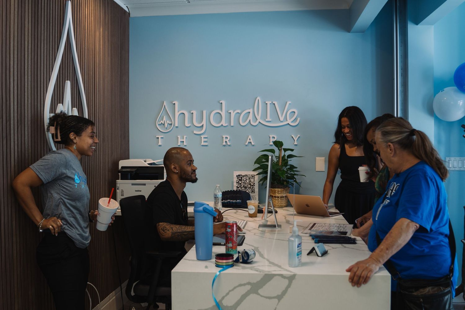 Staff members gather at the front desk inside HydraLive Therapy's modern blue and white reception area.