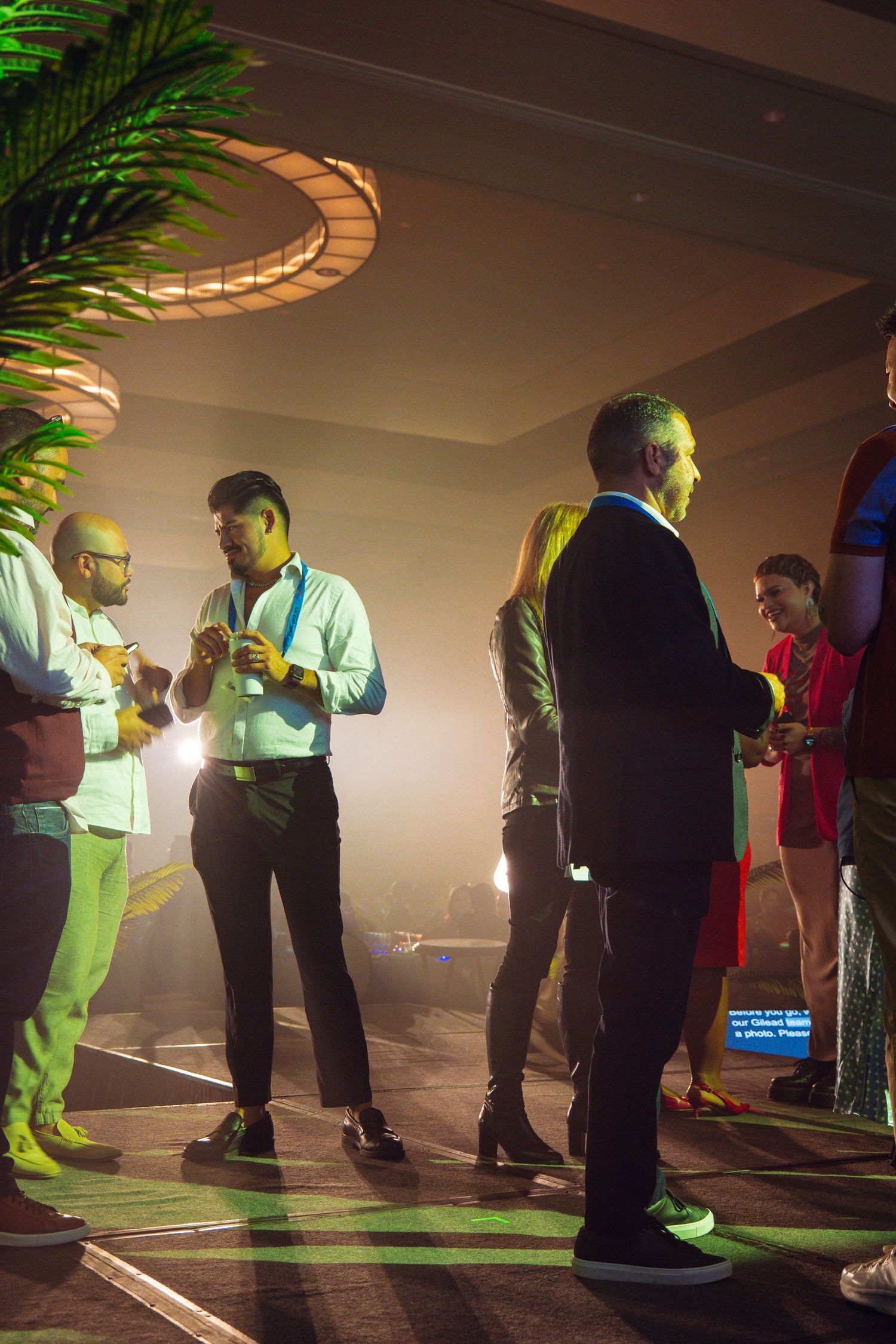 People socializing at an upscale evening event with atmospheric lighting, tropical decor, and a smoky ambiance.