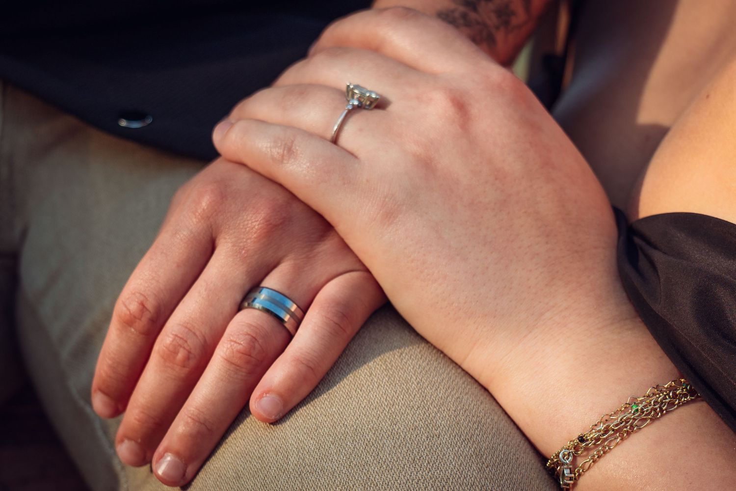 Couple holding hands showing engagement ring and wedding bands, symbolizing love and commitment.