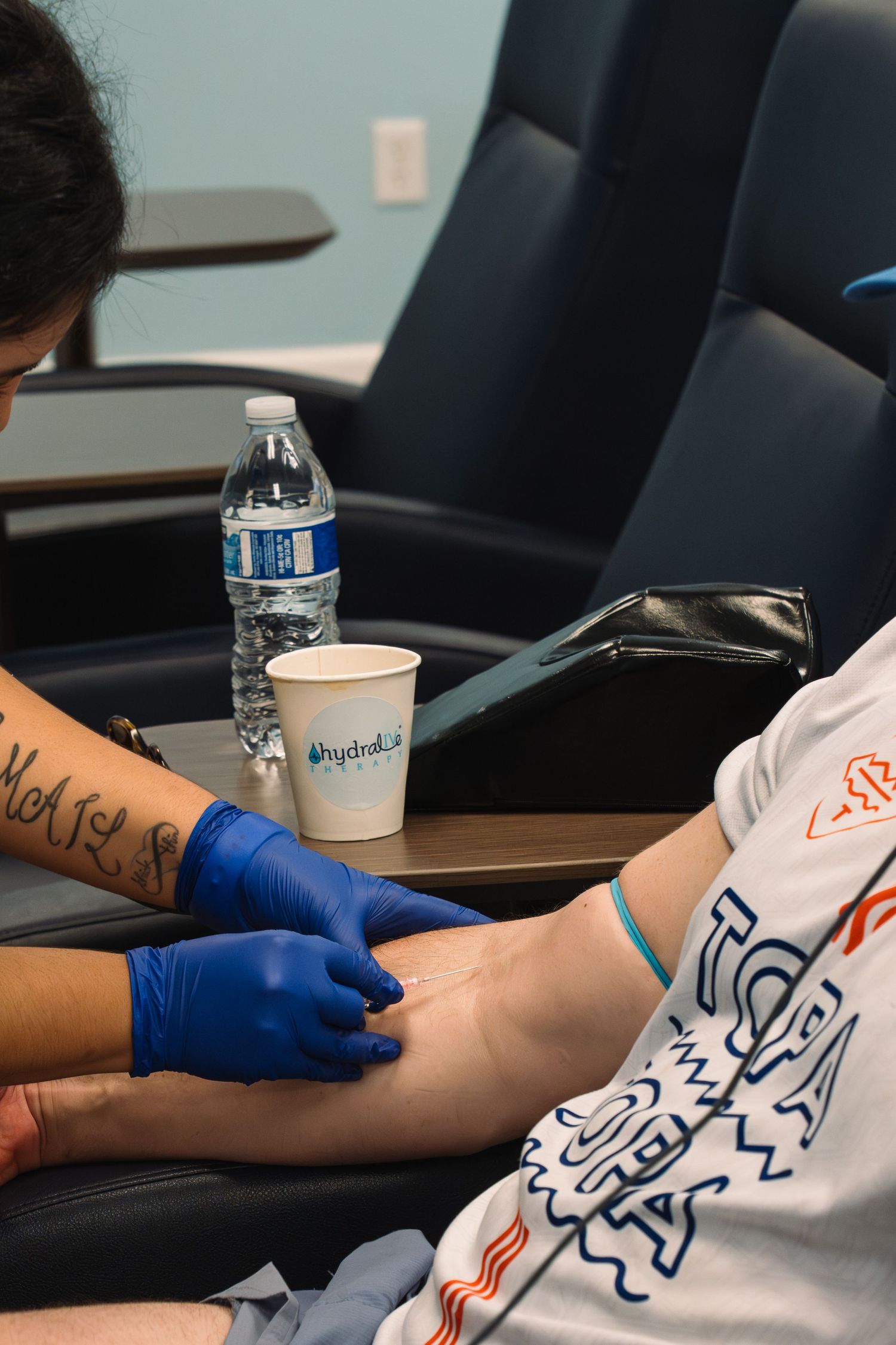 Medical professional in blue gloves drawing blood from a patient's arm at a hydration clinic.