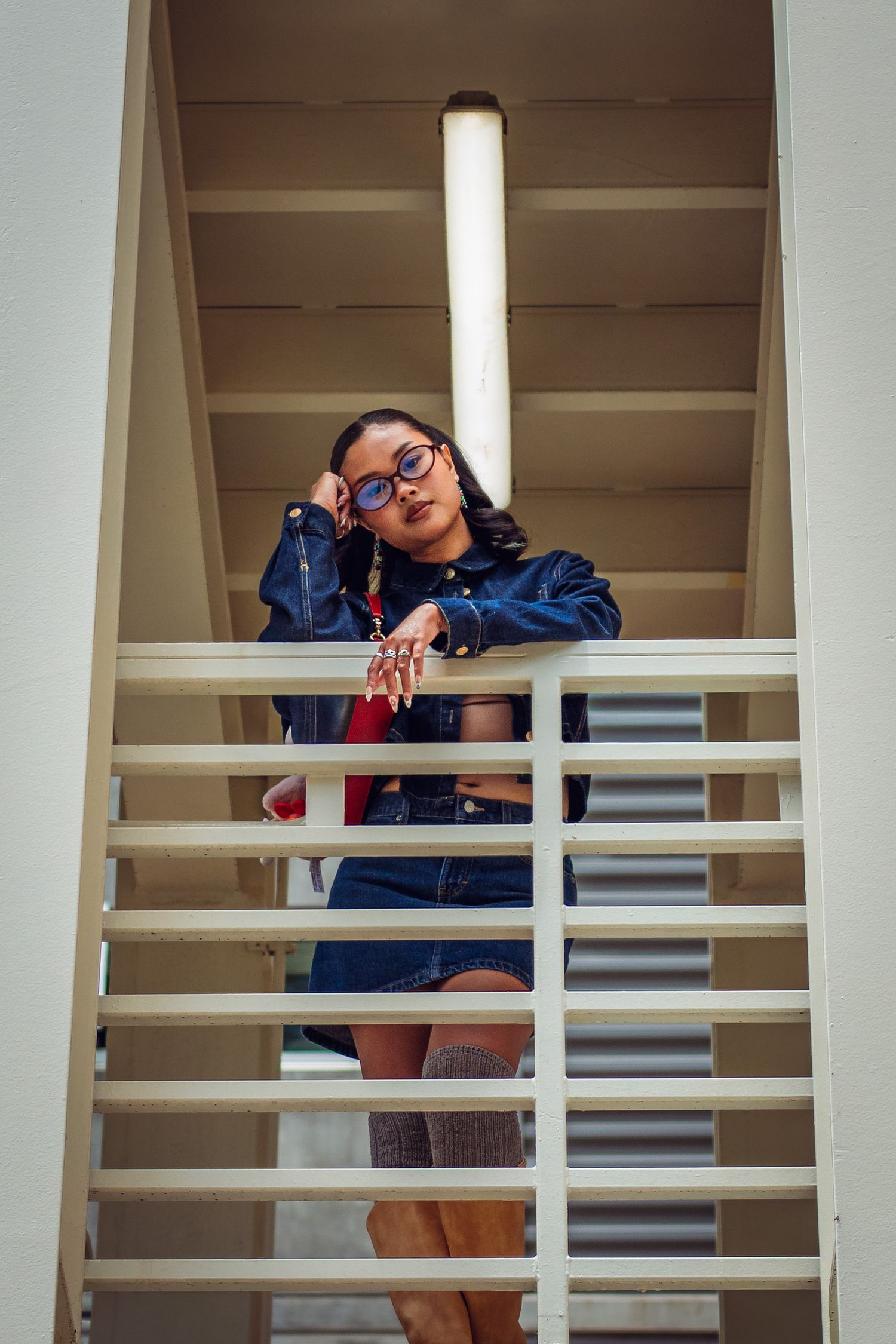 Young woman in glasses and denim outfit posing on outdoor stairs with white railings.