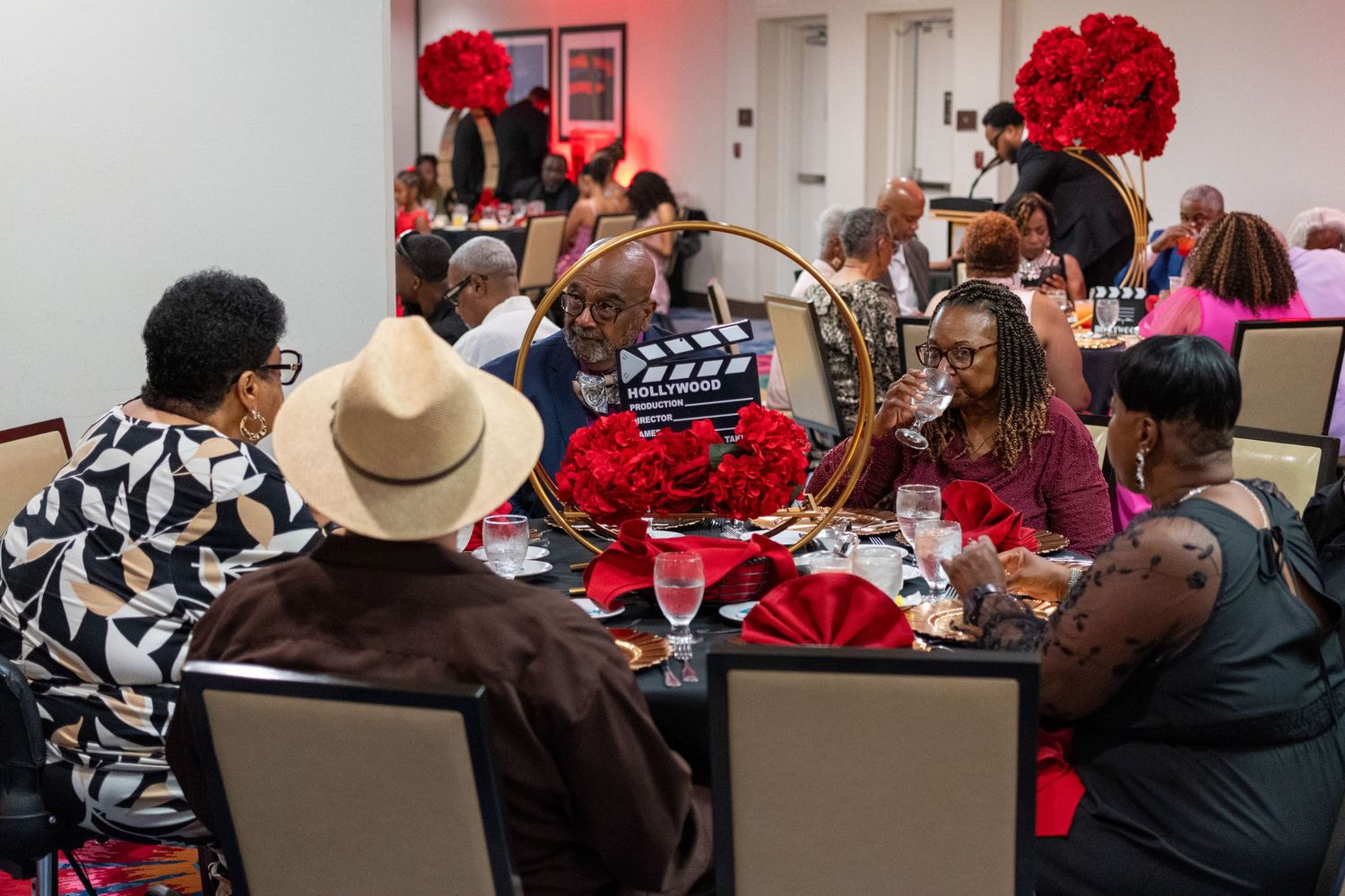 Elegant banquet hall with guests dining at tables adorned with red roses and decorative centerpieces during a formal event.