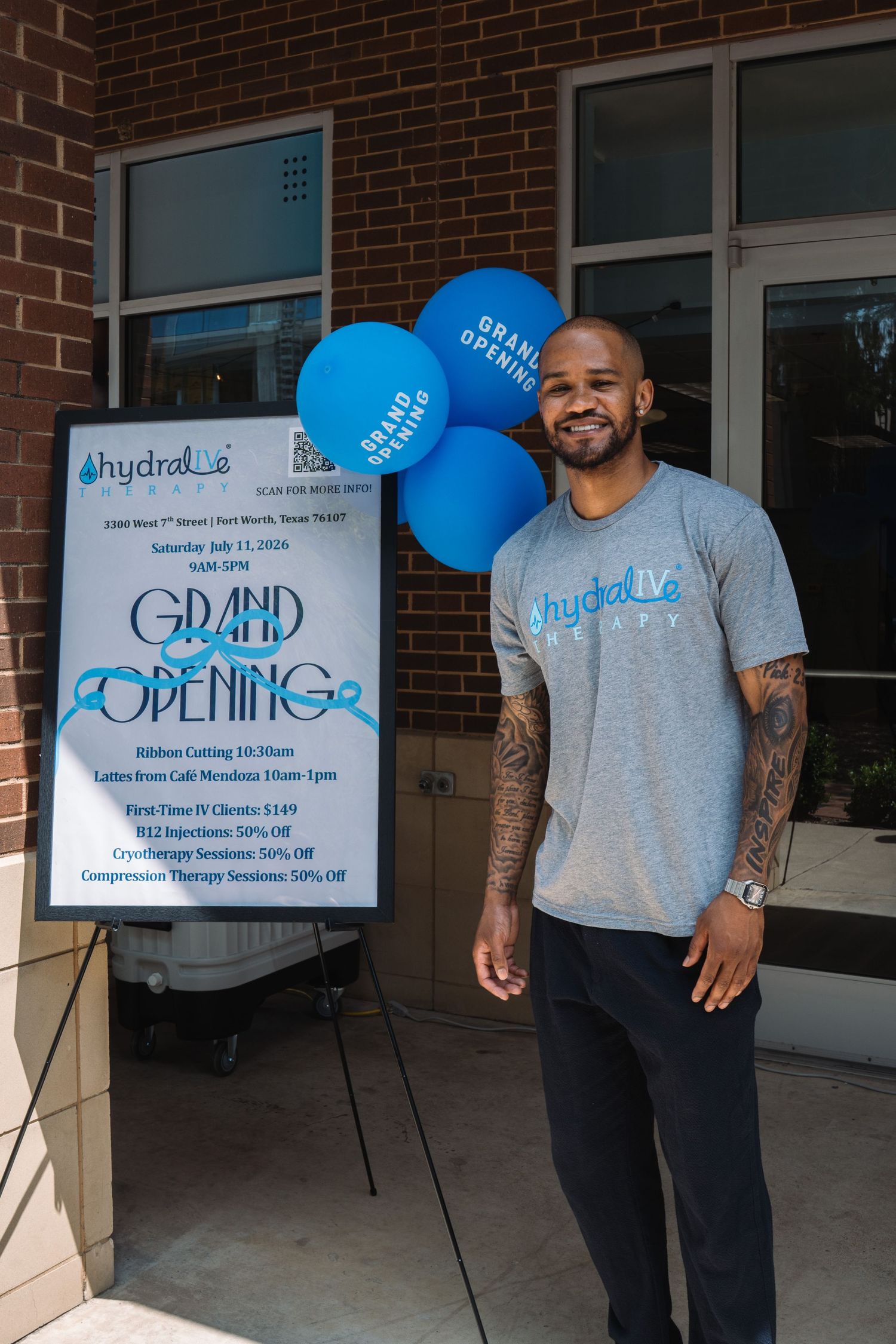 Man in Hydraline shirt smiling beside Grand Opening sign with blue balloons at Fort Worth location.