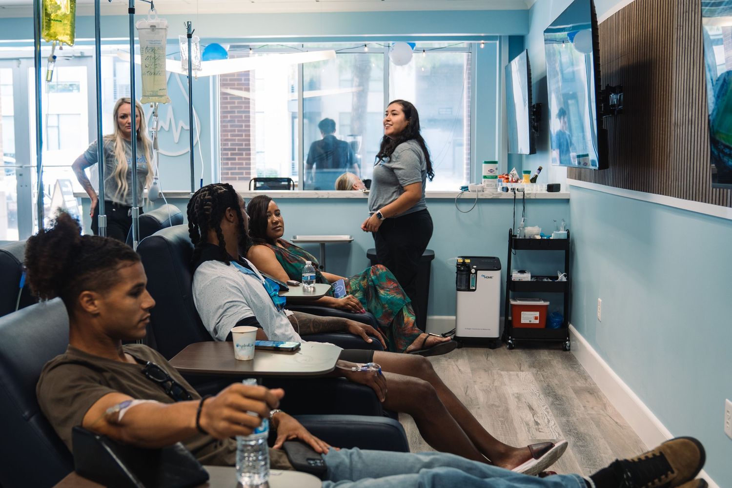 People relaxing in a modern IV therapy lounge with blue chairs, receiving treatments in a bright, welcoming clinic.
