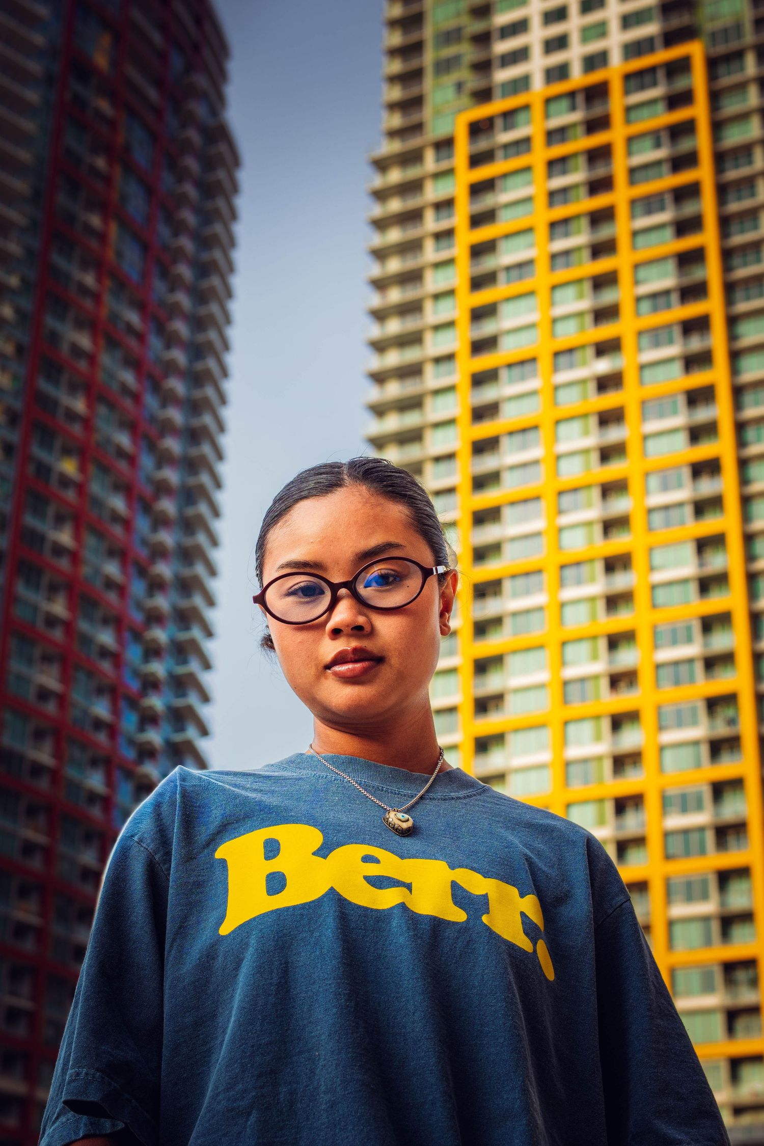 Young woman in blue Bern sweatshirt and glasses poses confidently in front of colorful high-rise buildings.