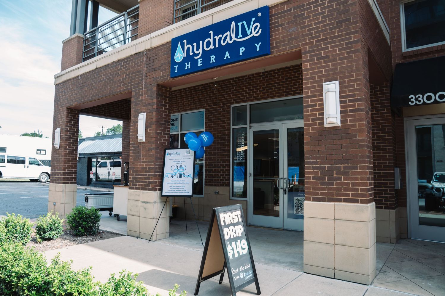 Exterior of HydraLive Therapy clinic with brick facade, glass doors, and a sidewalk sign offering first drop for $119.