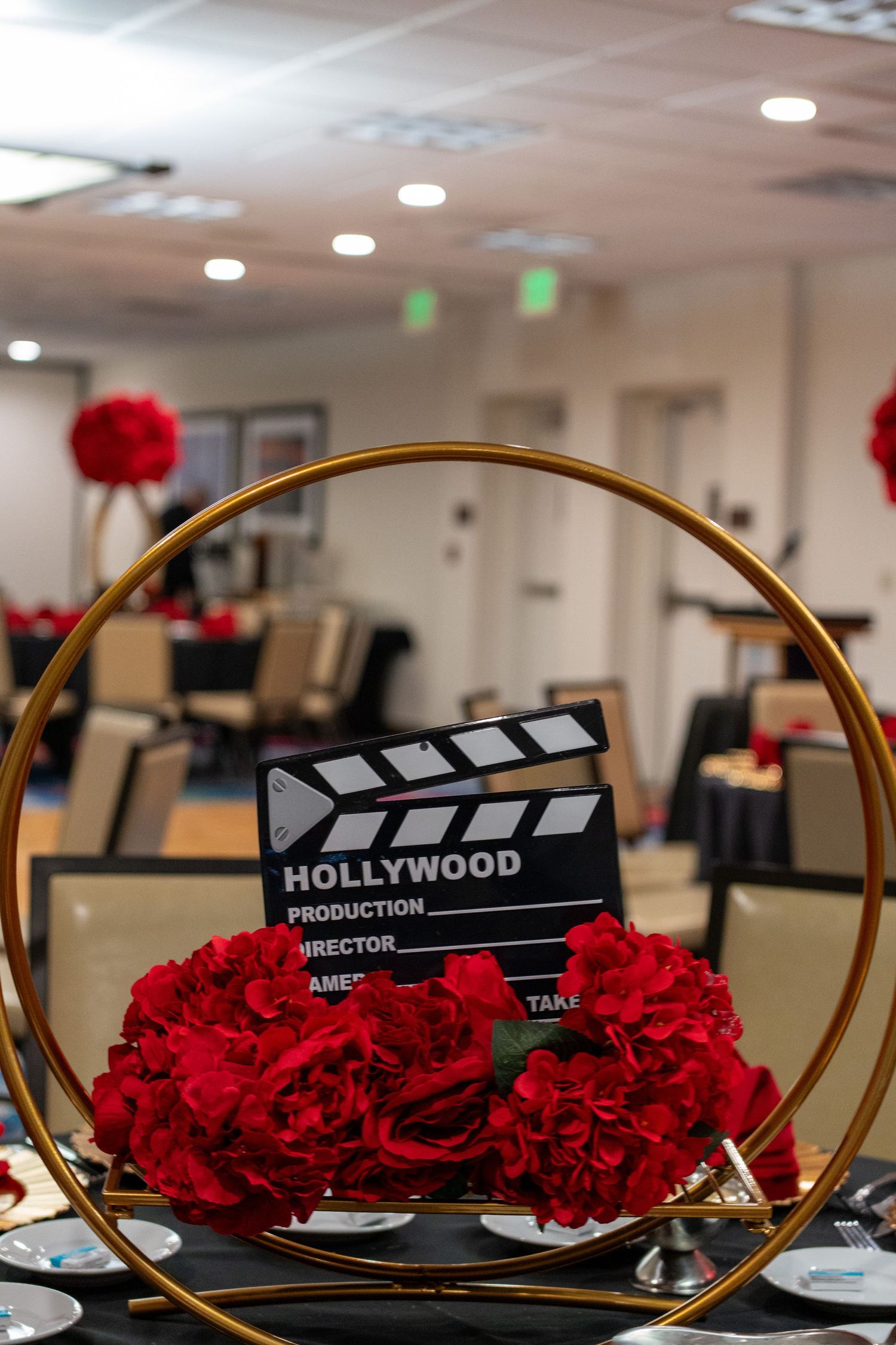 Hollywood clapperboard centerpiece with red roses in gold hoop, elegant event decor.