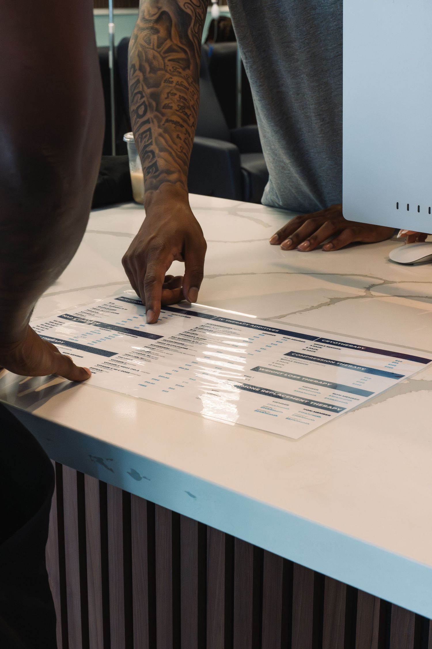 Tattooed man pointing at documents on a white marble reception desk in a modern office setting.