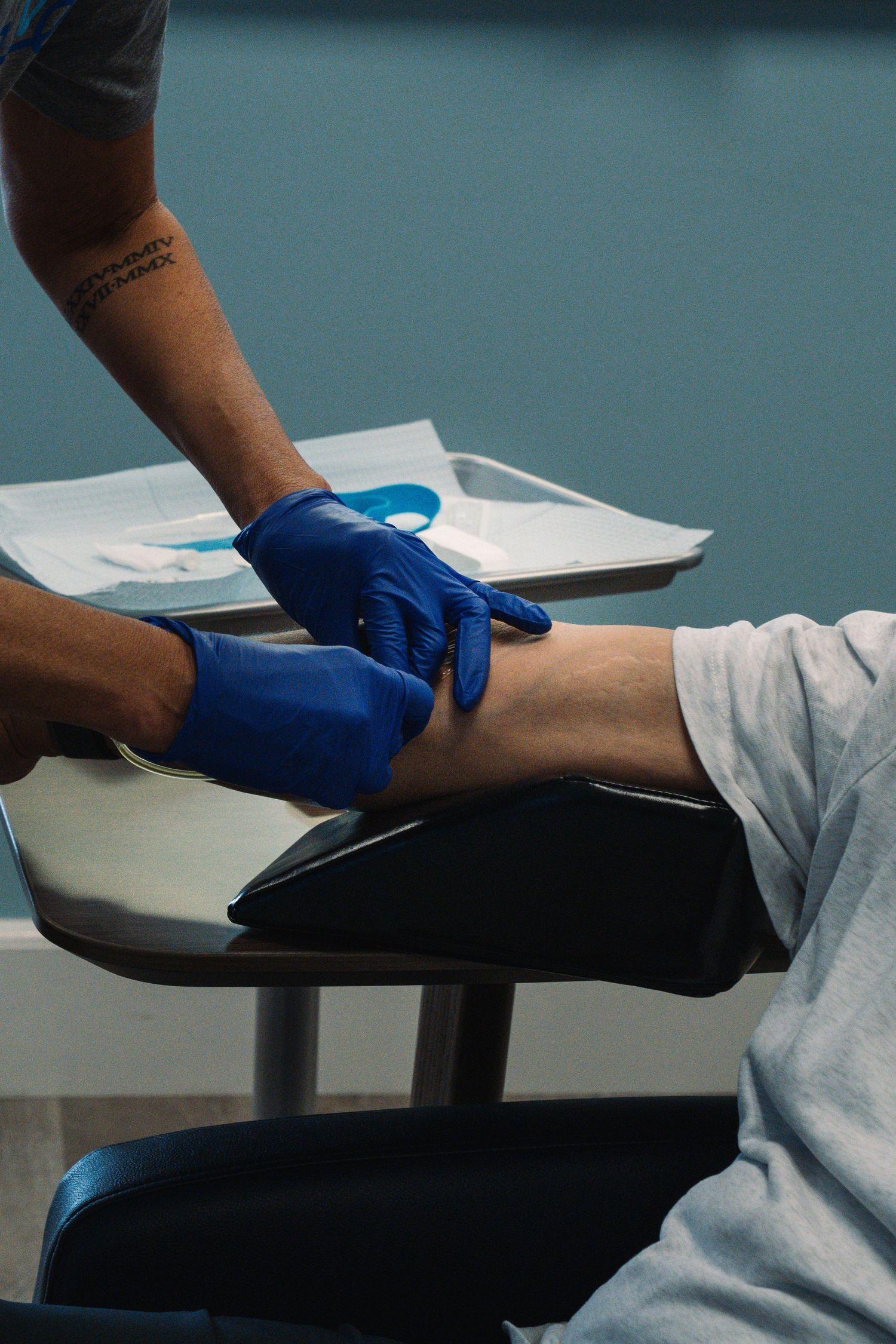 Medical professional in blue gloves preparing to draw blood from a patient's arm in a clinical setting.