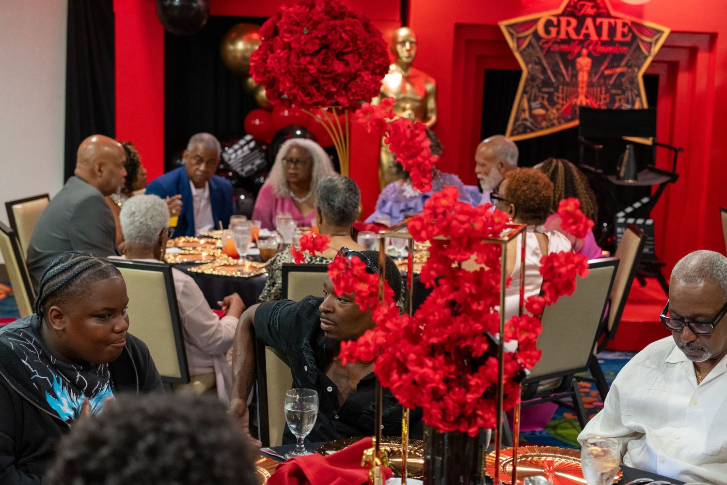 Elegant gala dinner with guests seated at tables adorned with red floral centerpieces and gold Oscar statuettes.