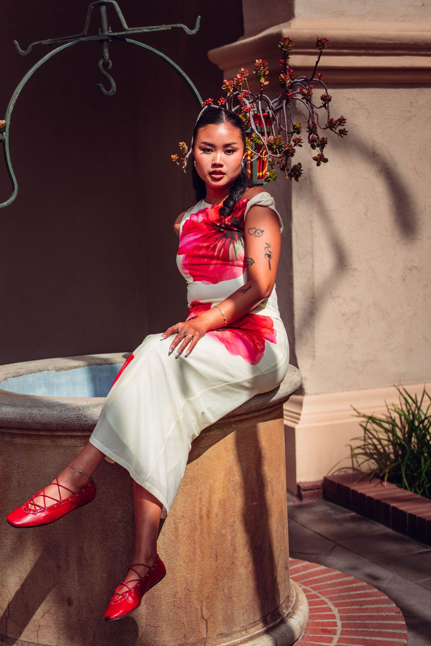 Young woman in red and white outfit sitting on a stone fountain with floral hair accessories.