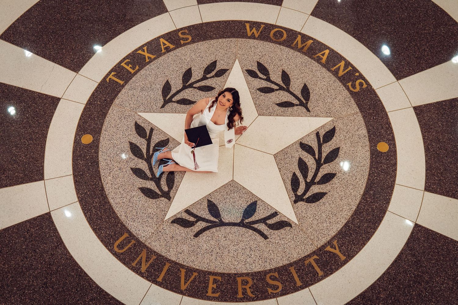 Woman posing on Texas Woman's University decorative floor seal with lone star emblem in grand building.