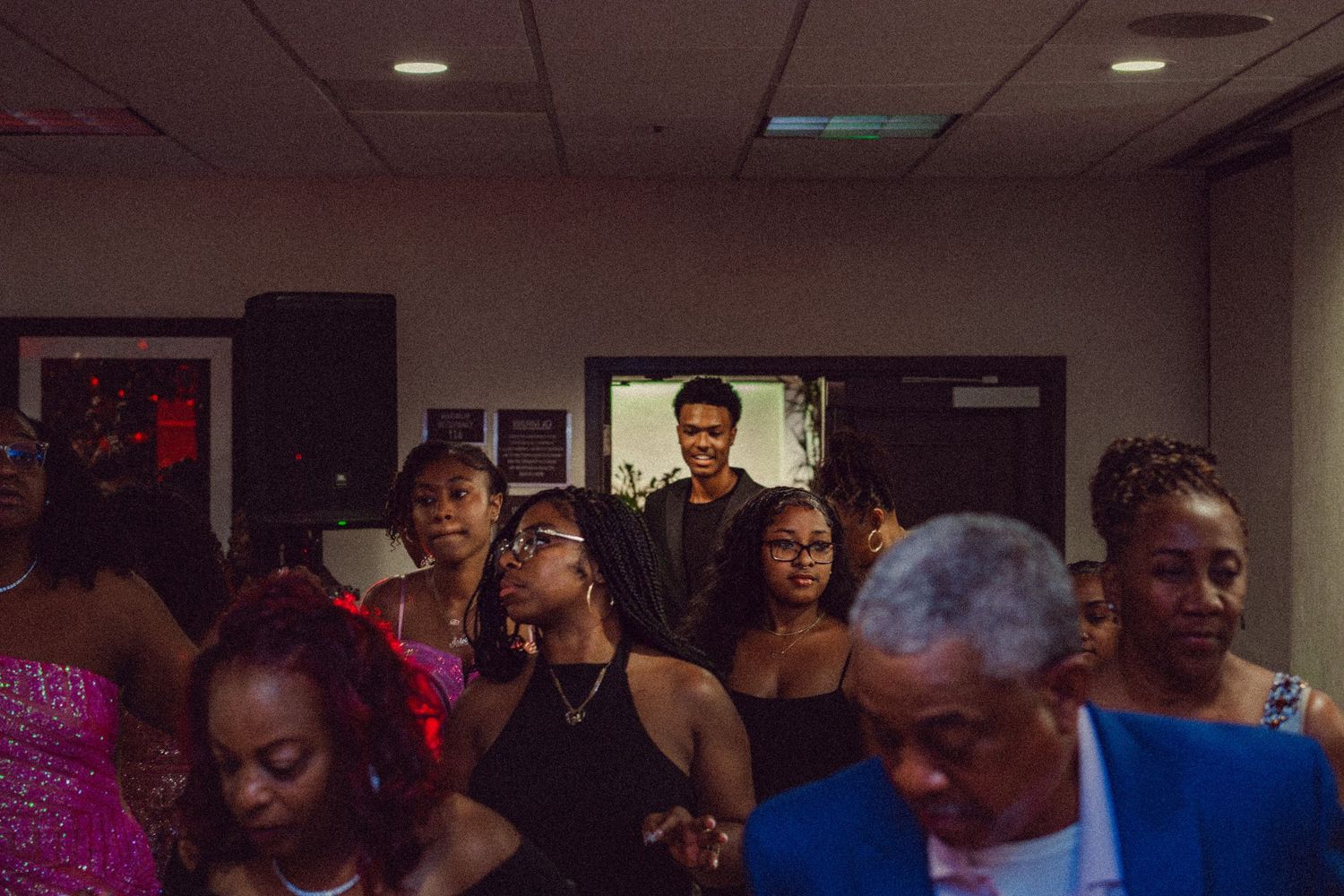 A diverse group of elegantly dressed people gathered at a formal event or prom celebration indoors.