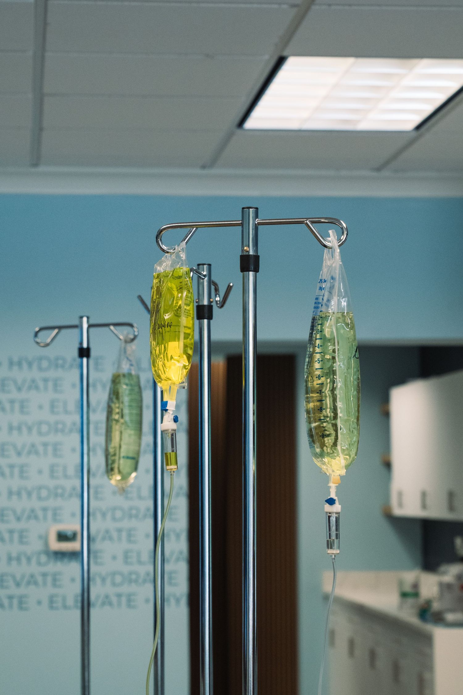 IV drip bags hanging on medical poles in a hydration therapy clinic with teal walls.