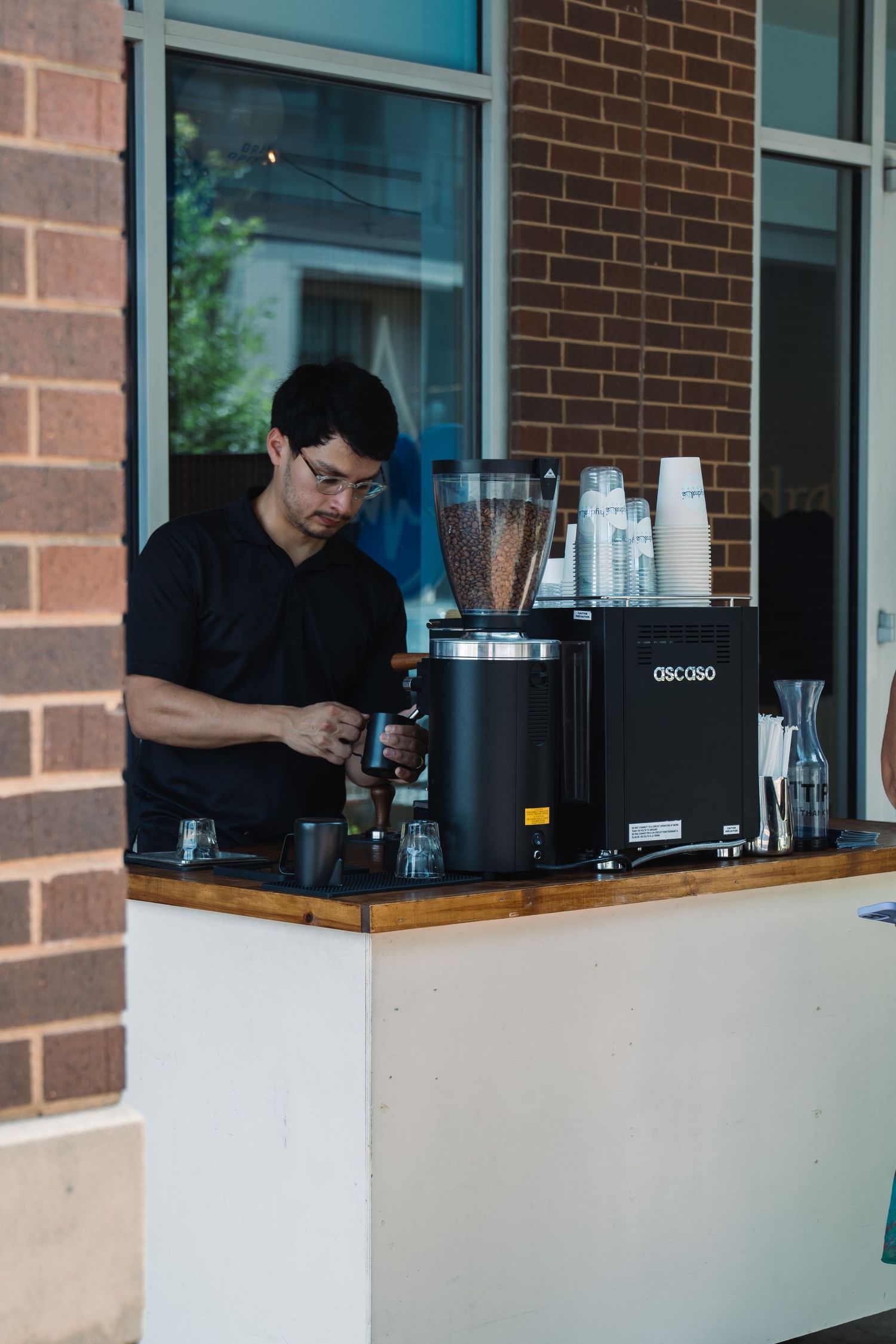 Barista in black shirt preparing coffee at an outdoor espresso bar with OSCOSO equipment.